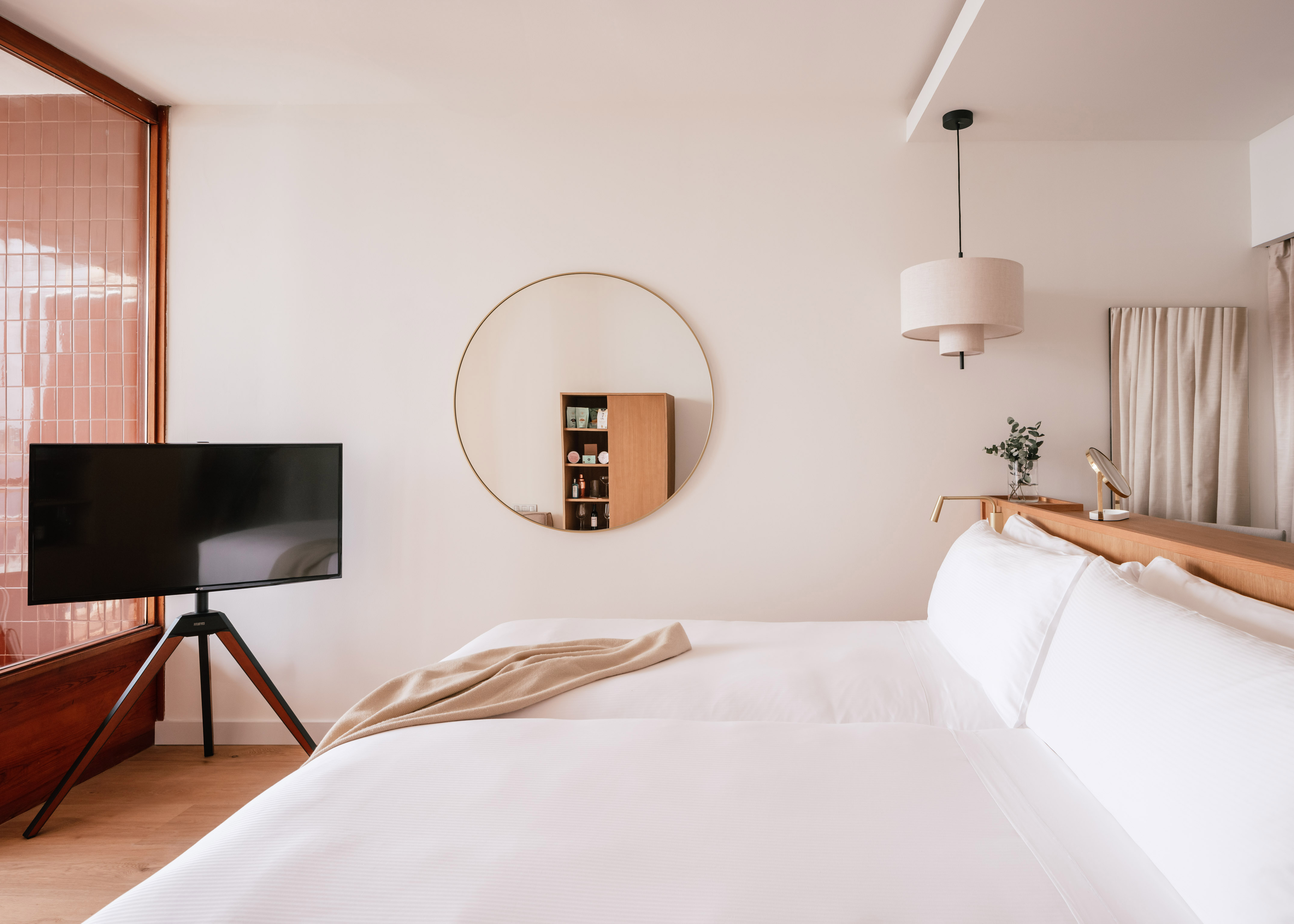 Modern hotel bedroom with white bed, tripod TV, and gold-framed mirror.