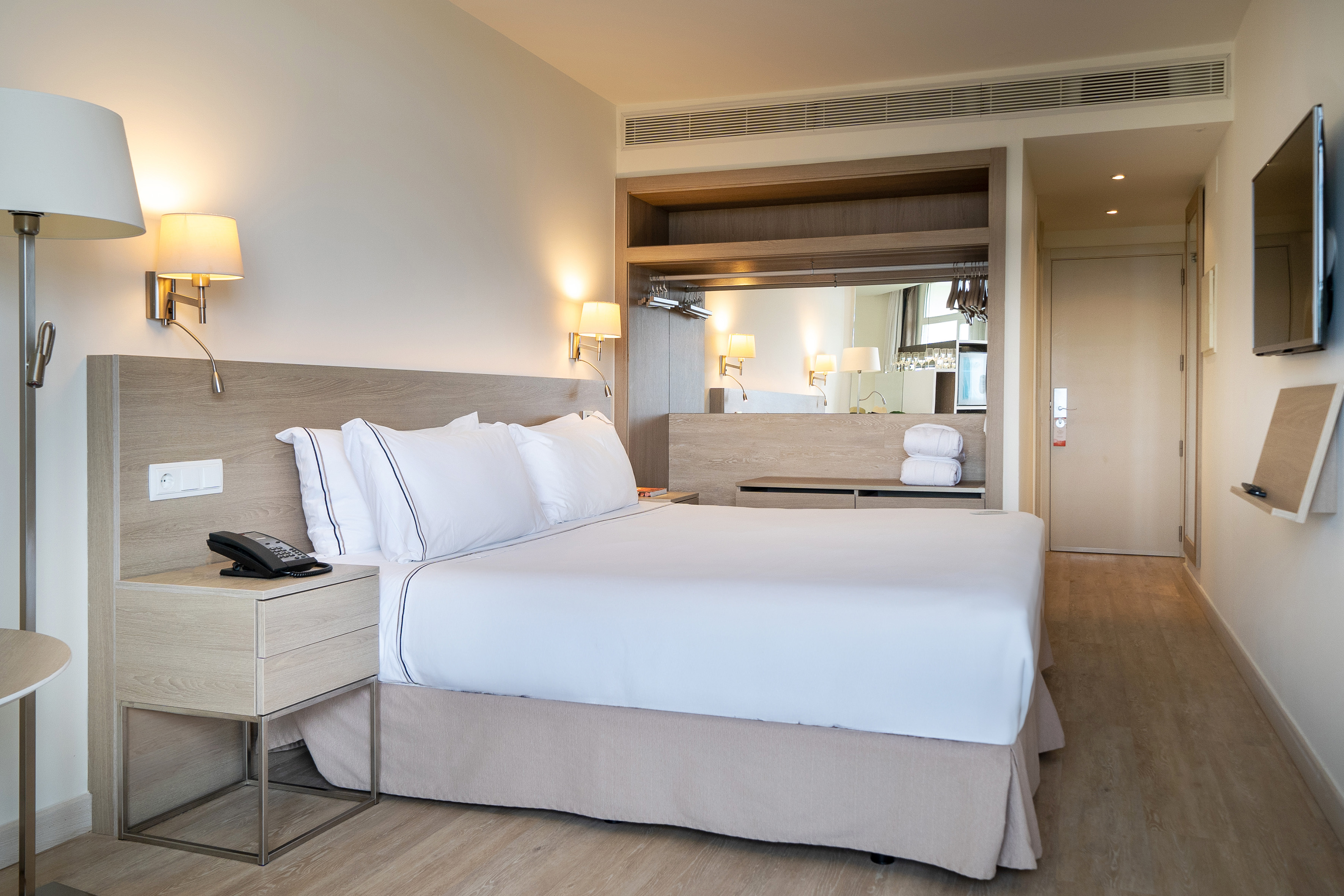 Clean hotel bedroom featuring a large white bed and light wood furniture.