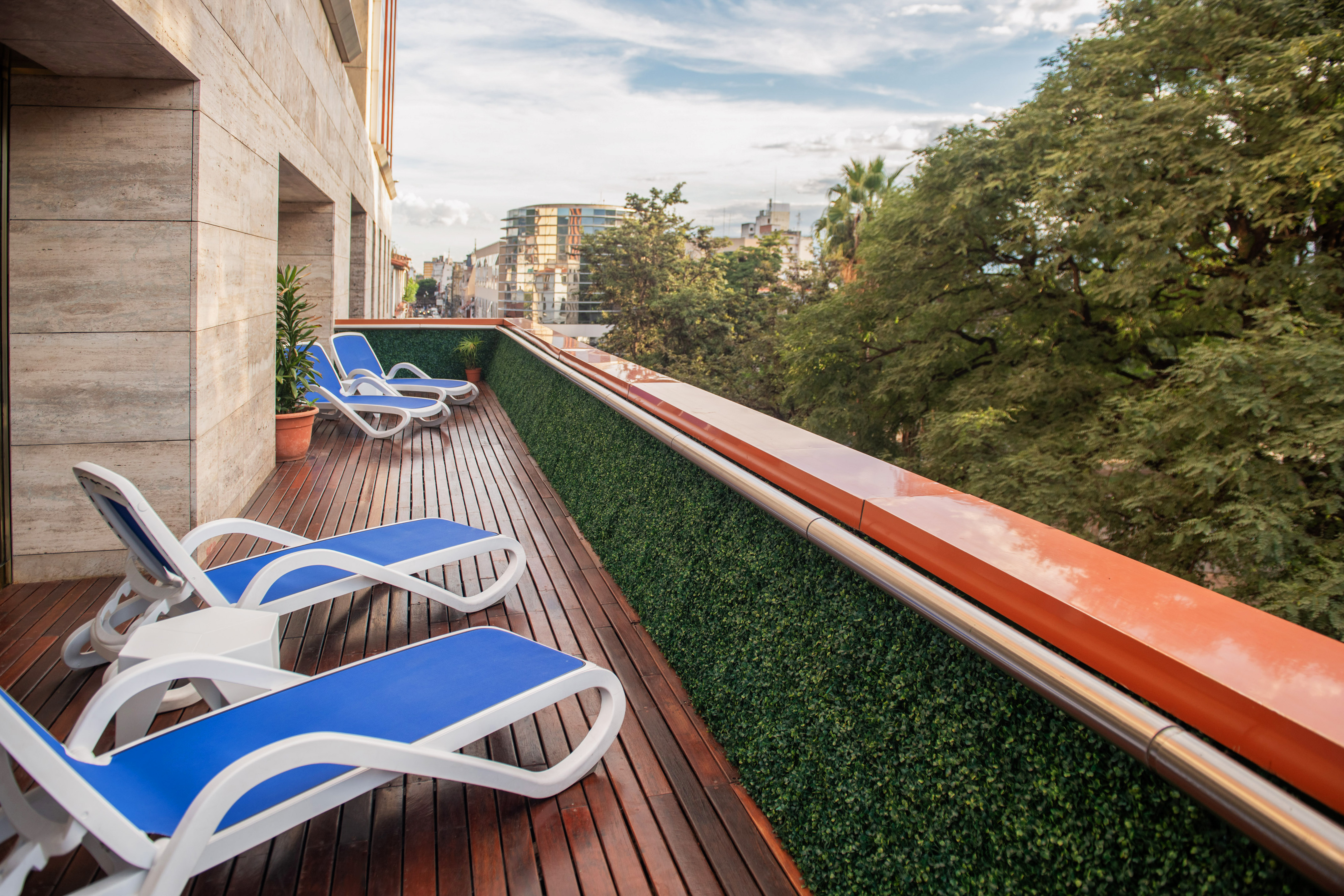 Hotel terrace with blue lounge chairs, wooden deck, green wall, city view.