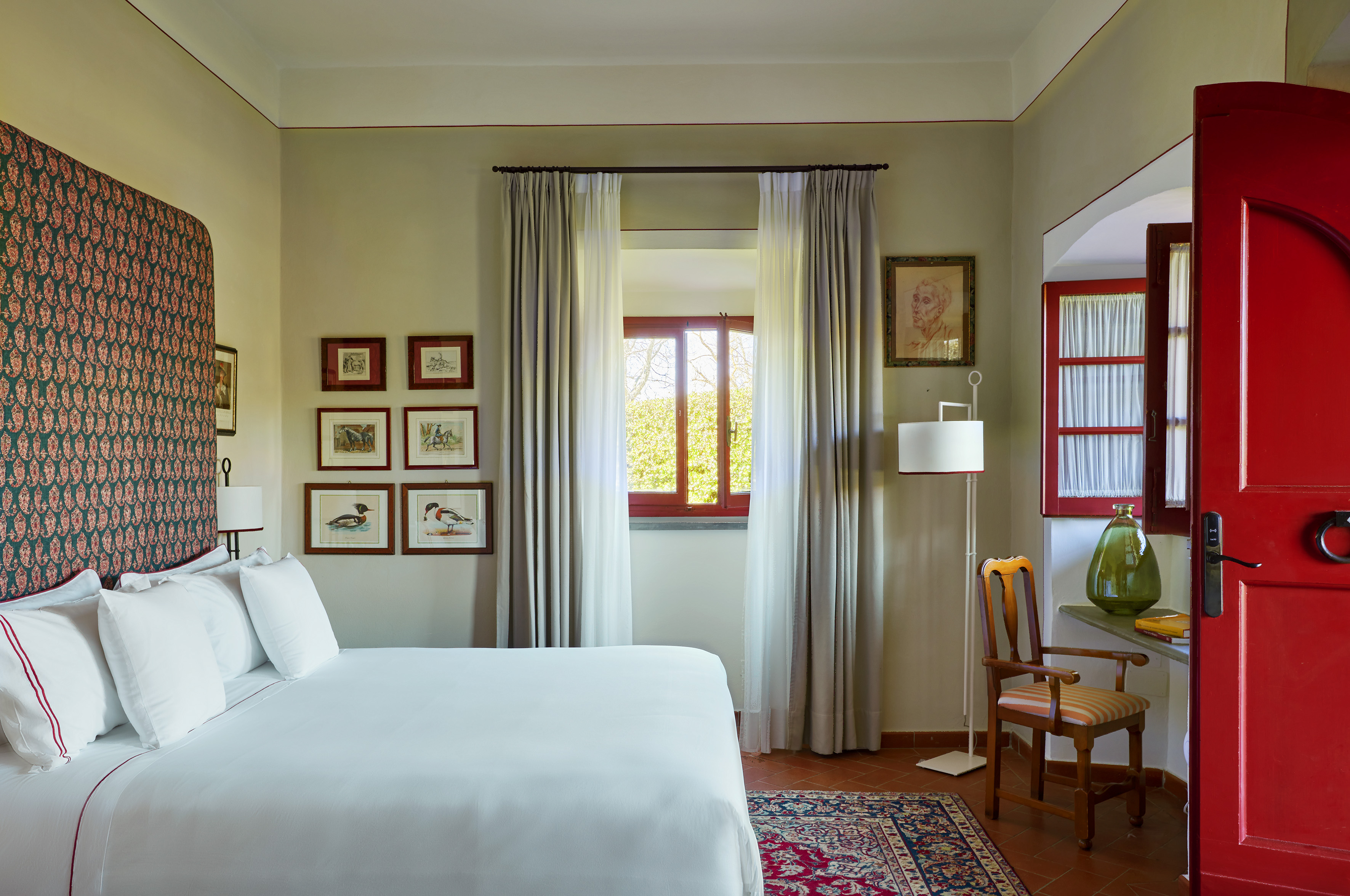 Stylish hotel bedroom with white bed, red door, and framed artwork.