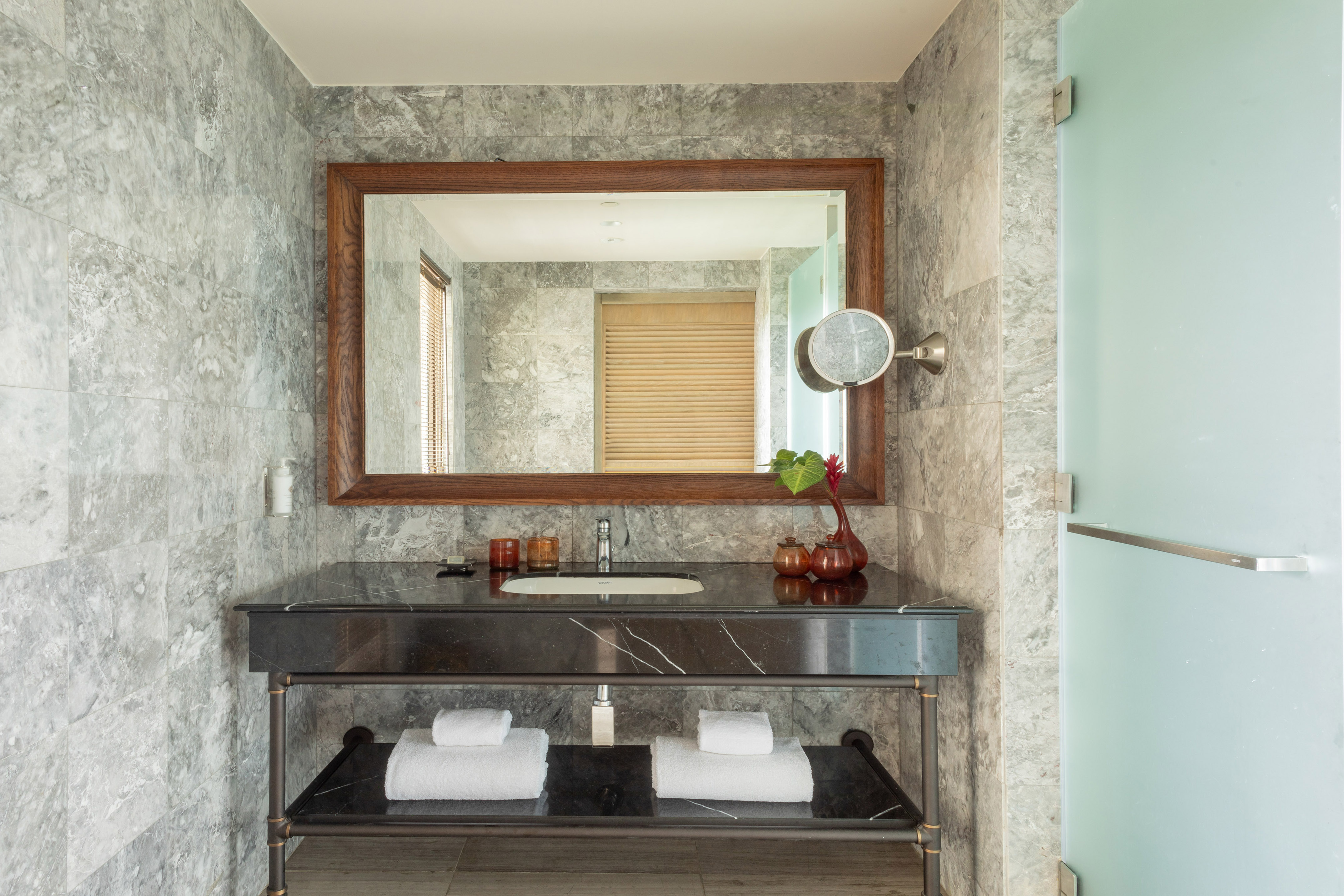 Modern bathroom vanity with black marble sink, wooden mirror, grey tiles.