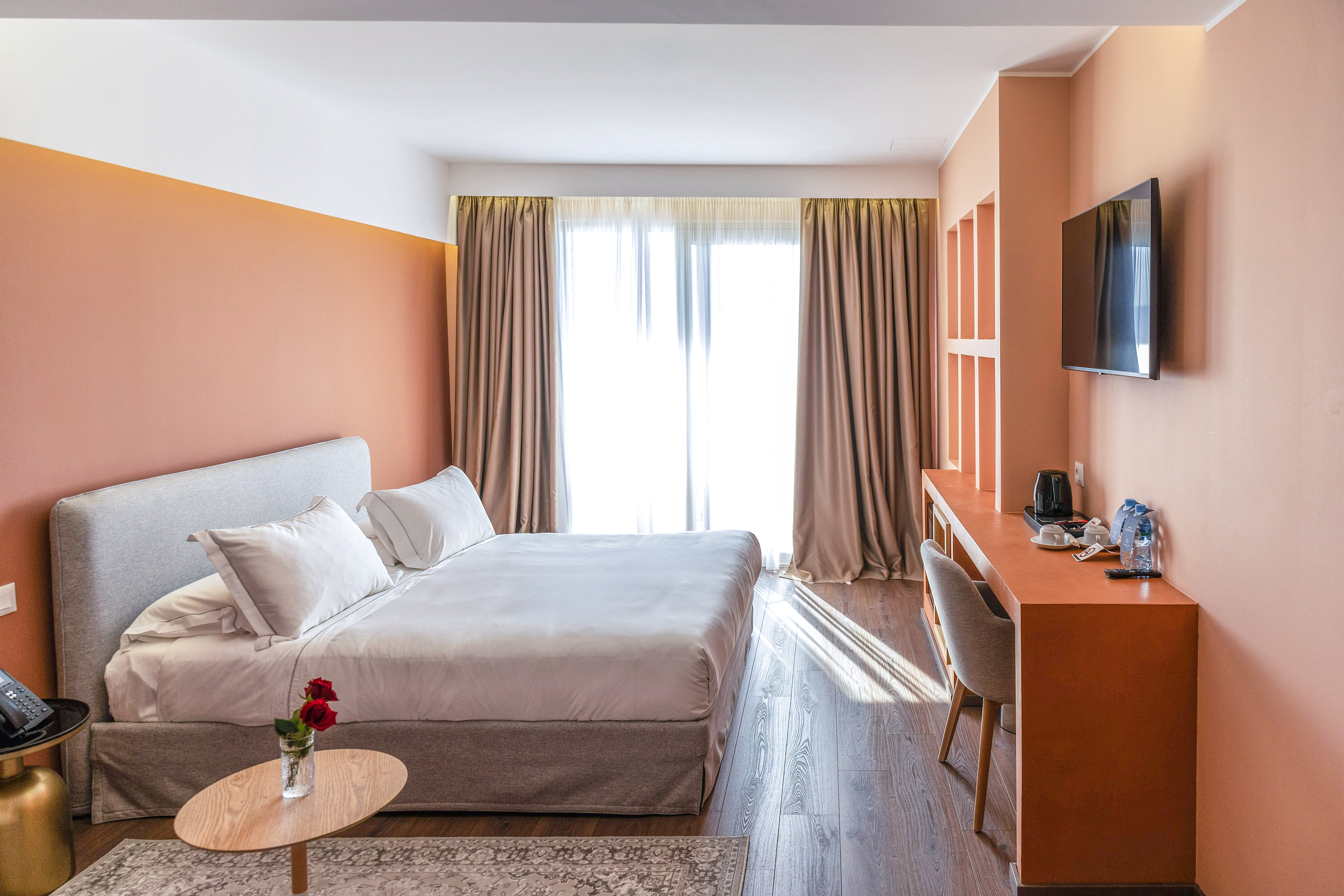 Bright modern hotel room with king bed, peach accent wall, large window, and desk.