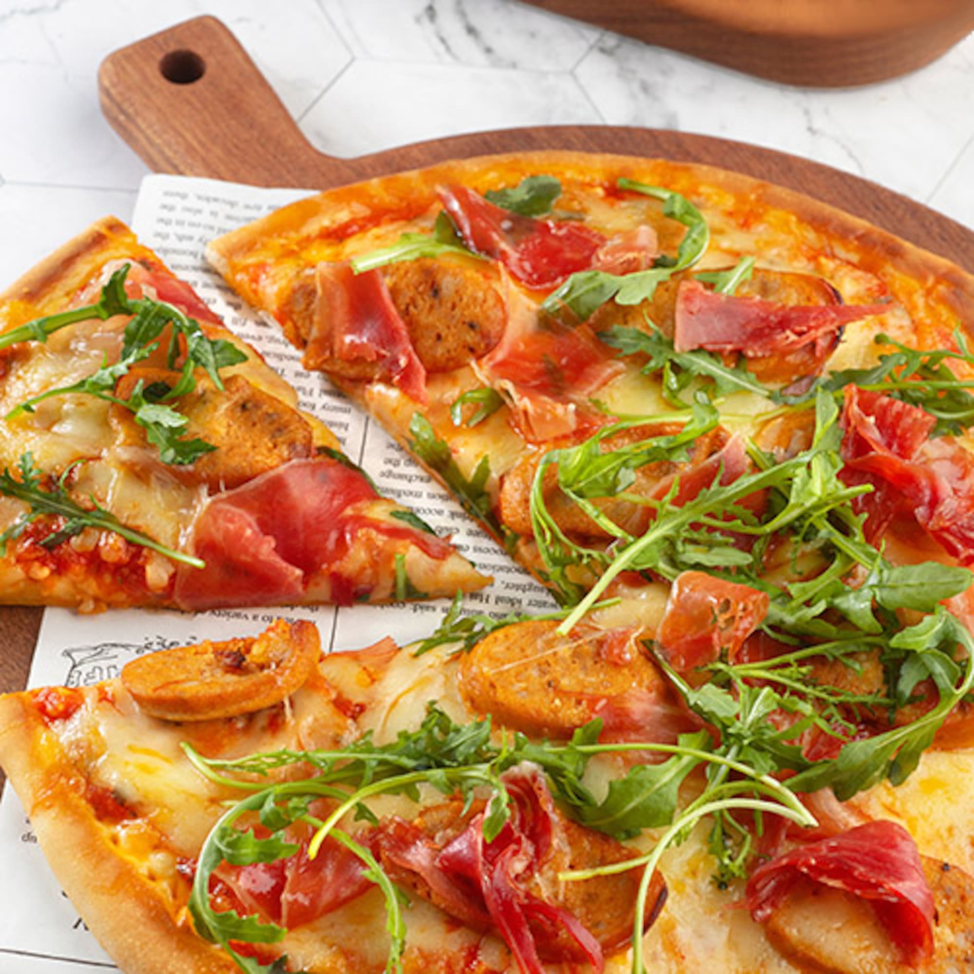 a pizza with meat and greens on a wooden board