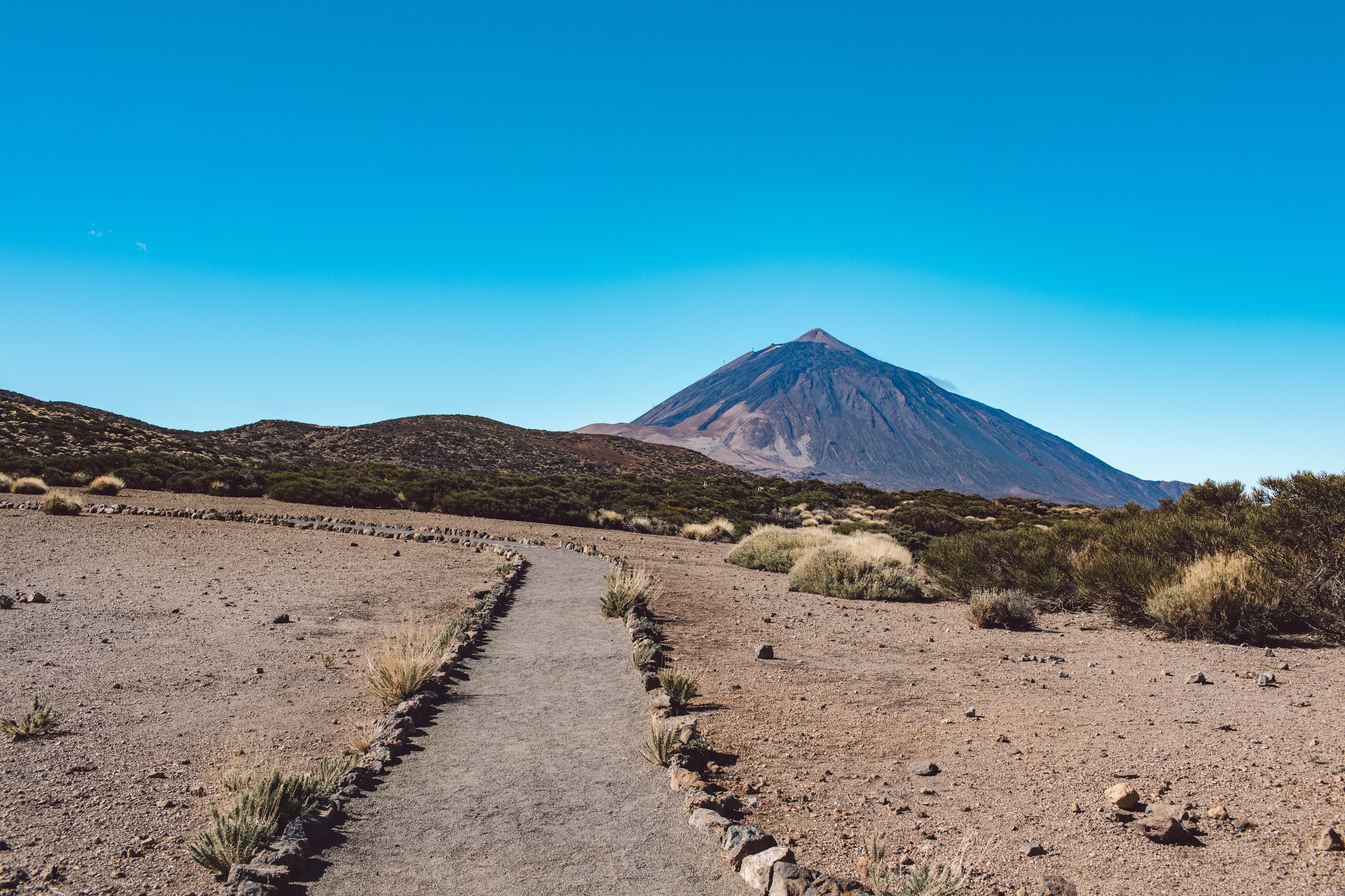 Gravel path to Teide volcano, clear blue sky over Tenerife volcanic landscape.