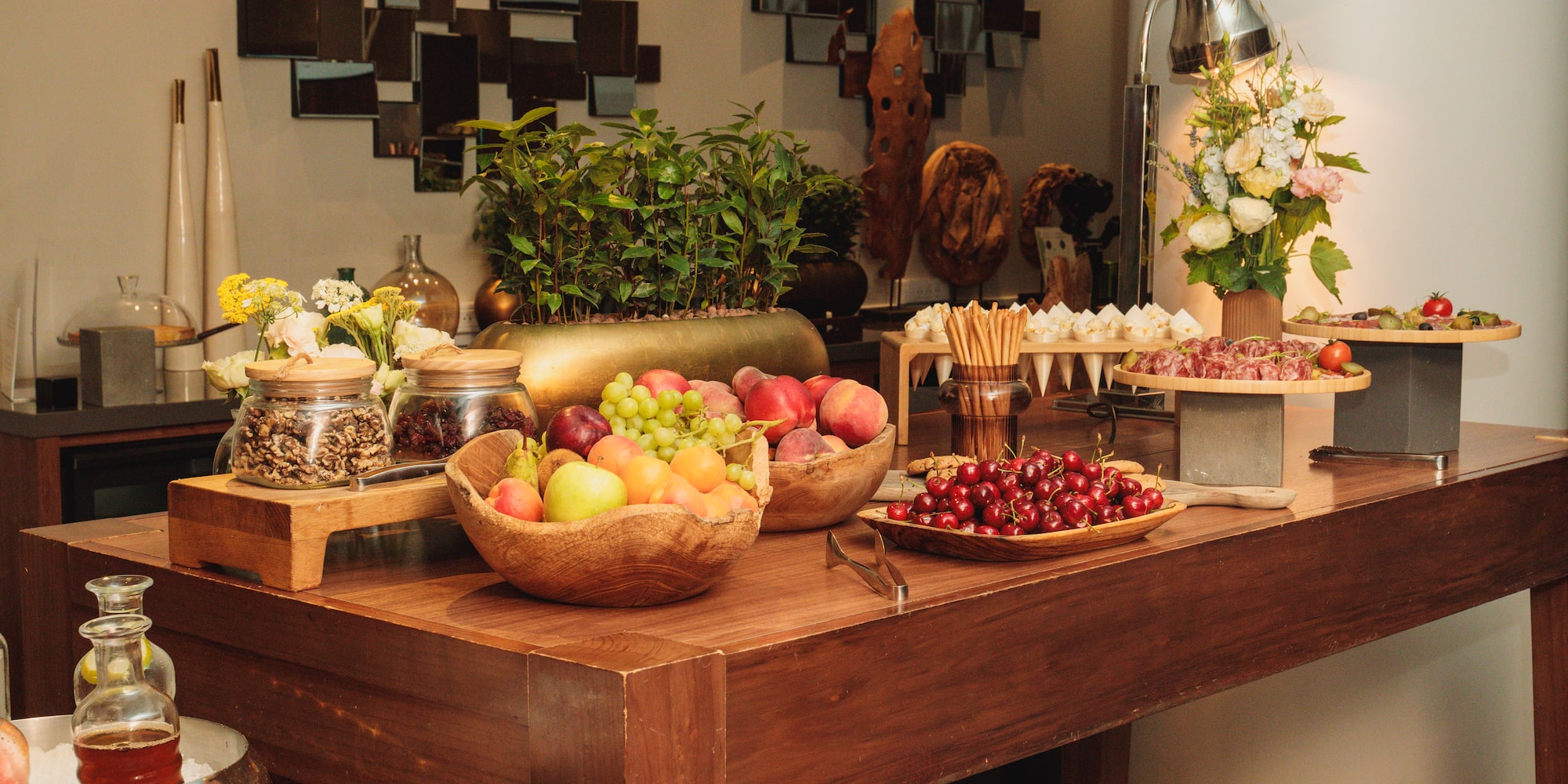Luxurious buffet table with fresh fruit, charcuterie, nuts, and floral decor.