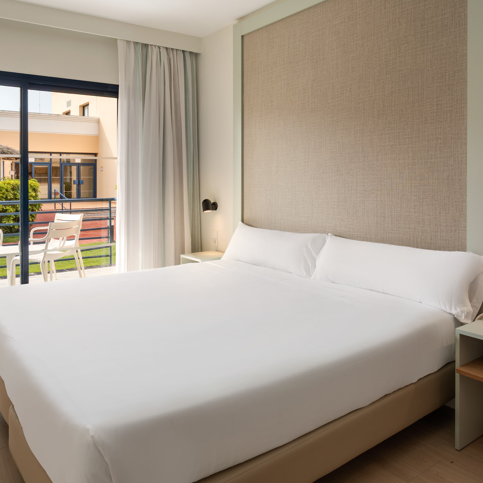 Hotel room with comfortable bed, balcony, and view of resort grounds.