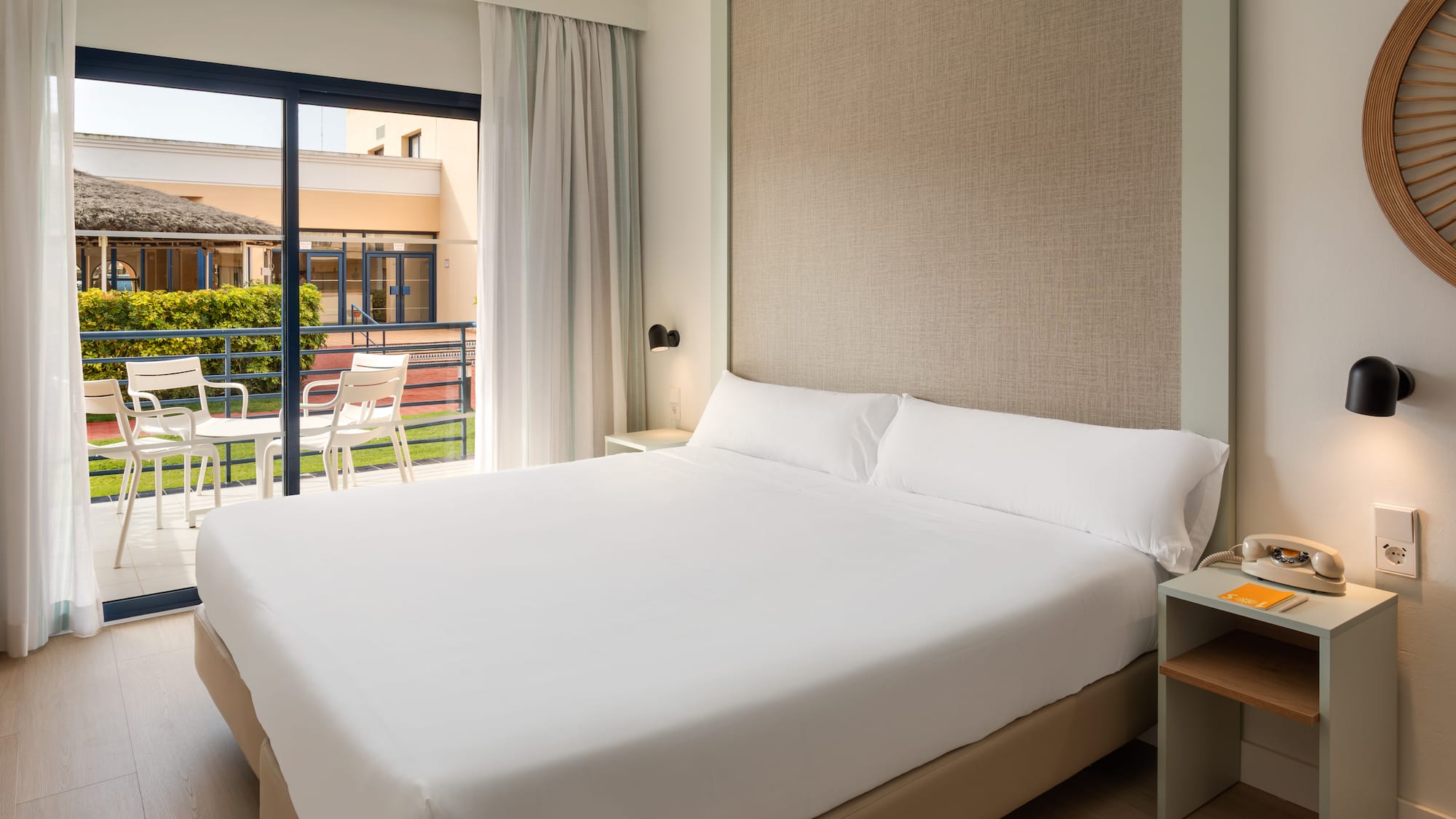 Modern hotel room with large bed, balcony, and green resort view.