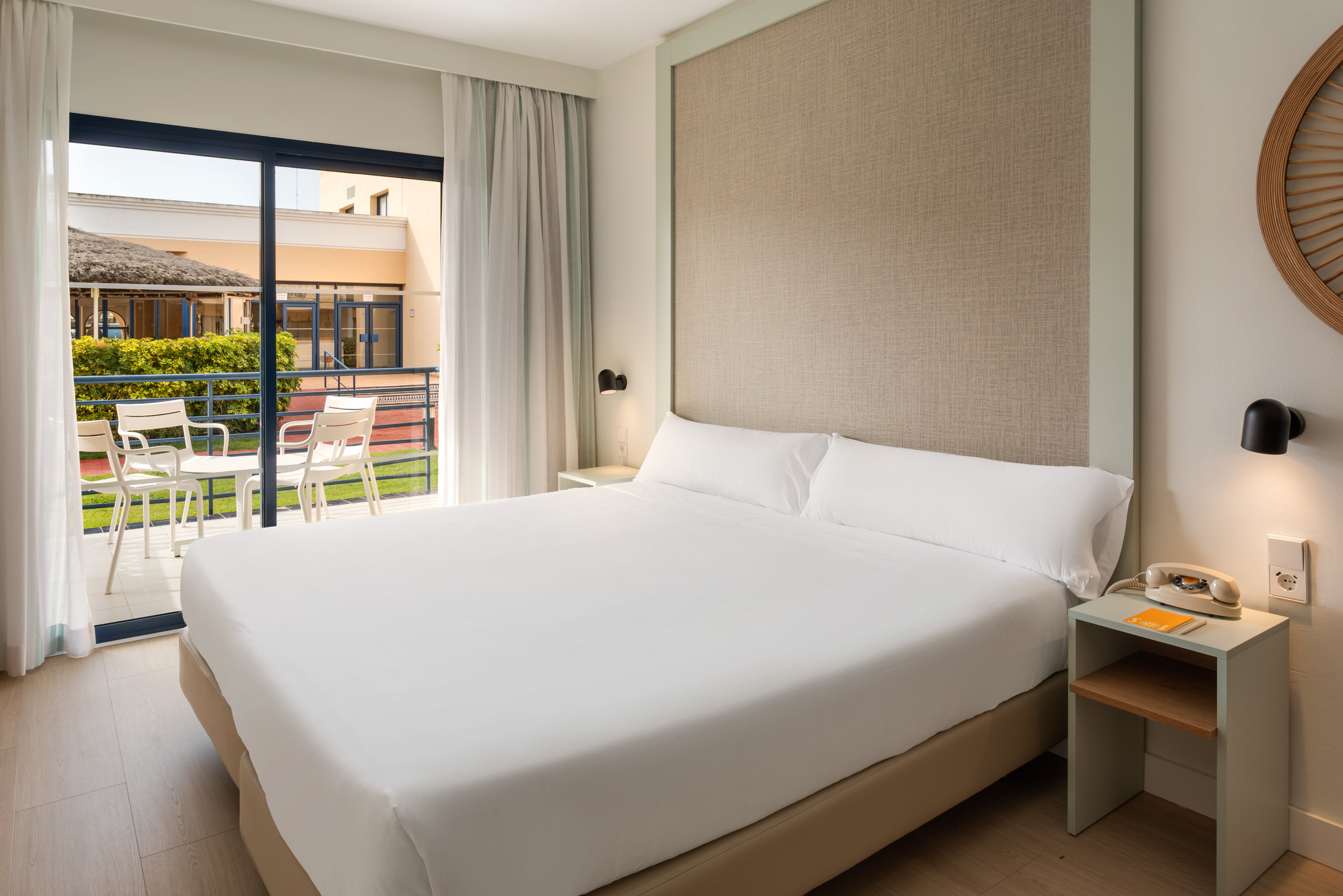 Modern hotel room with large bed, balcony, and green resort view.