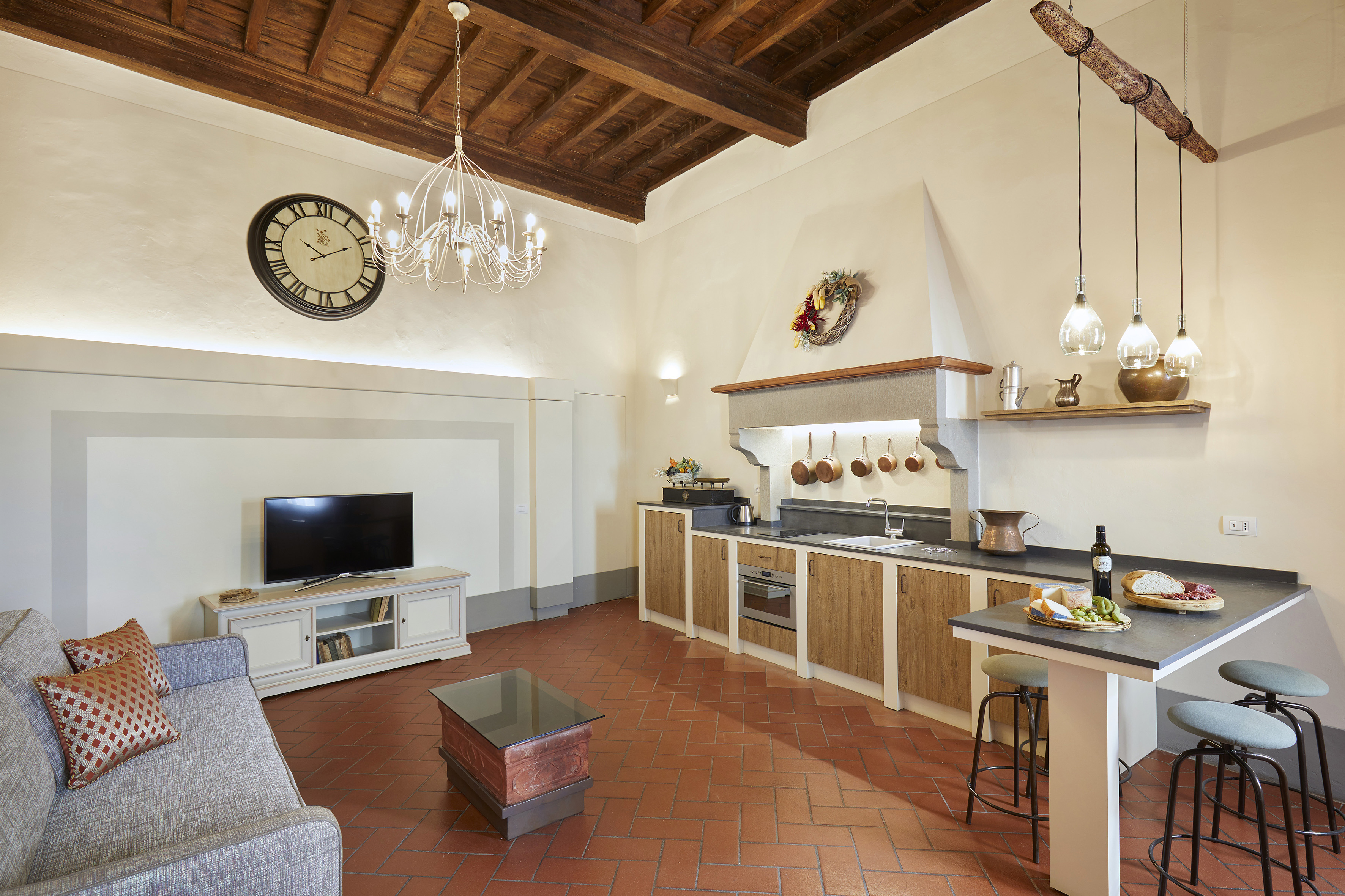 Rustic open plan kitchen and living room with terracotta floor, wood beams.