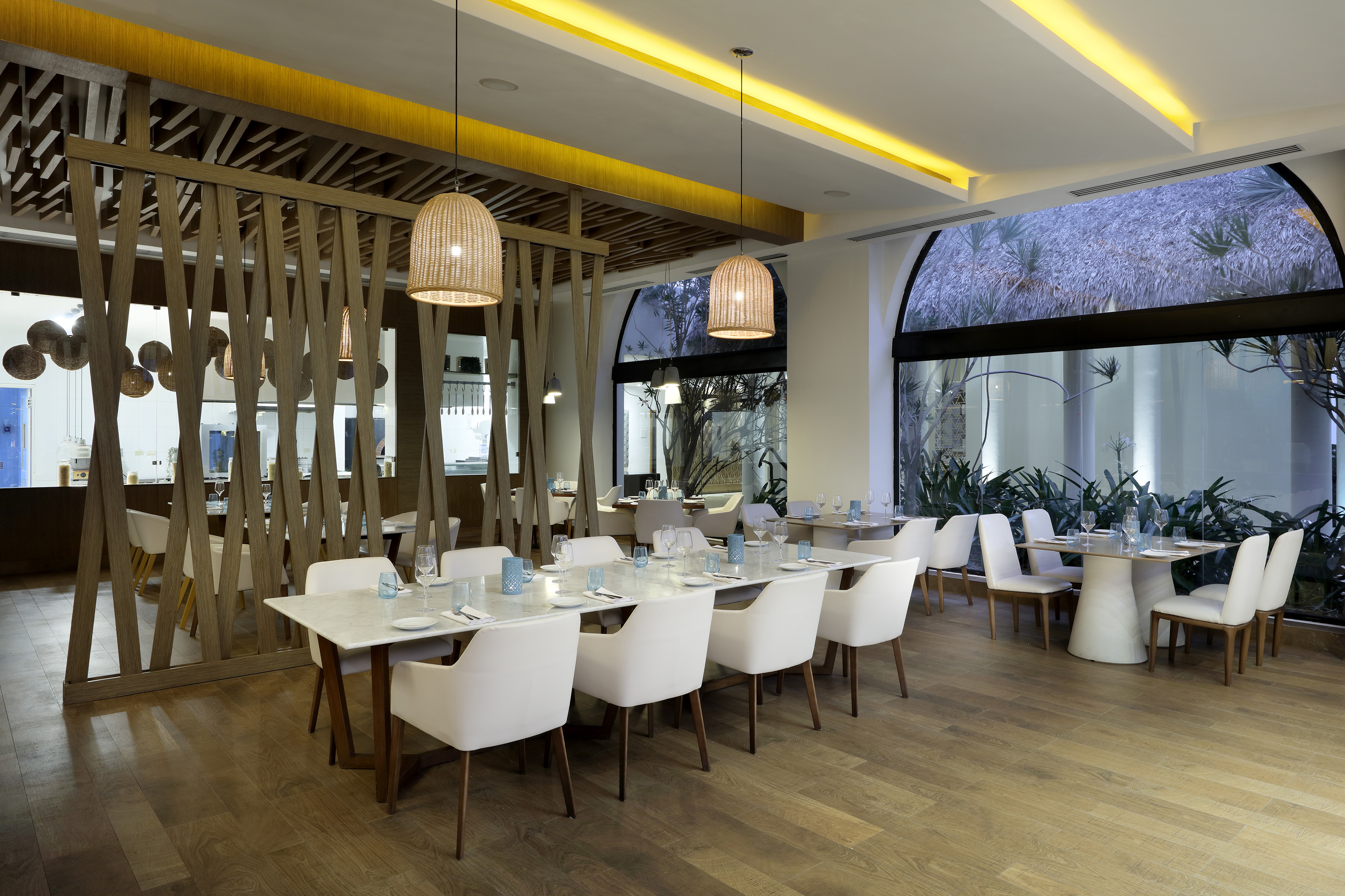 Modern restaurant dining room with white chairs, wood partition, and pendant lights.