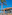 Ammos á la carte restaurant with palm tree, balcony, and clear blue sky.