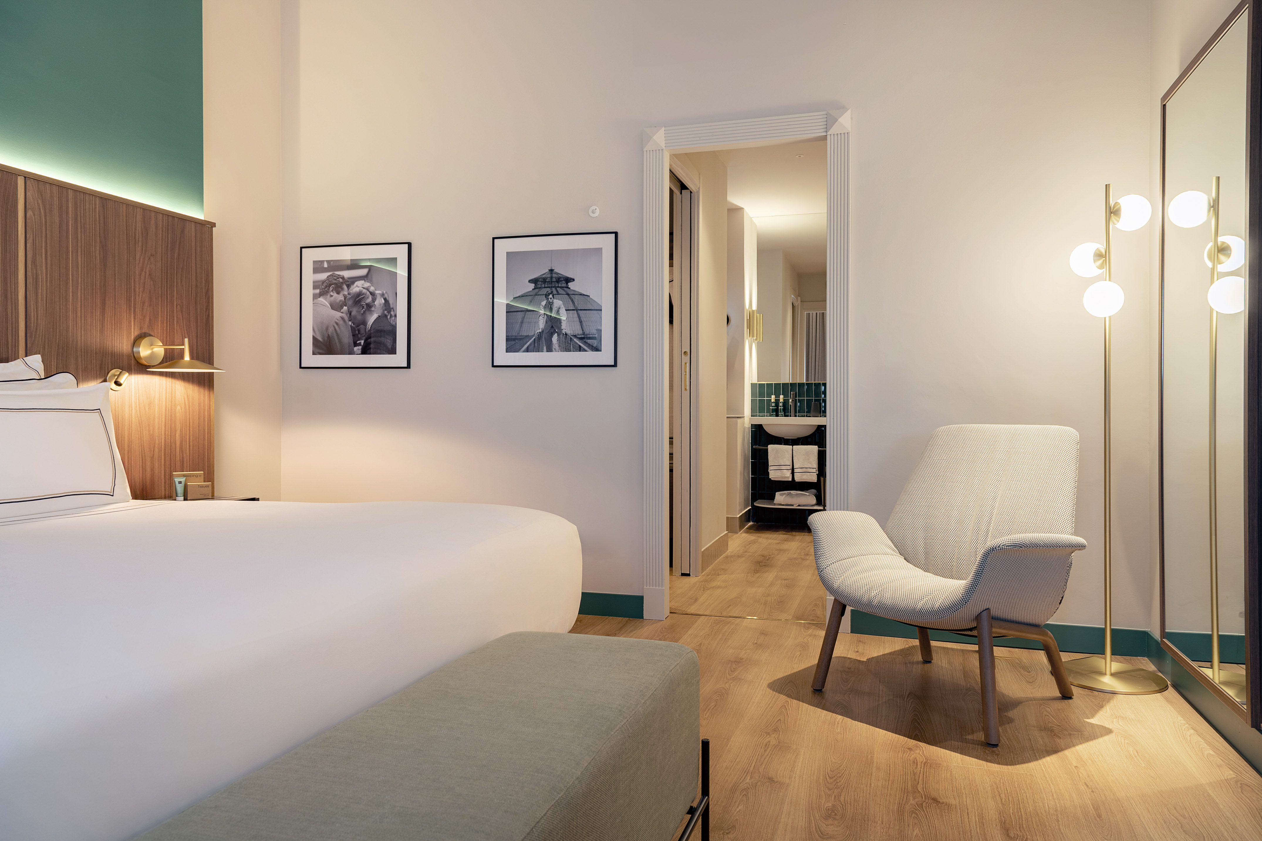 Modern hotel bedroom with white bed, chic armchair, and open view to the bathroom.