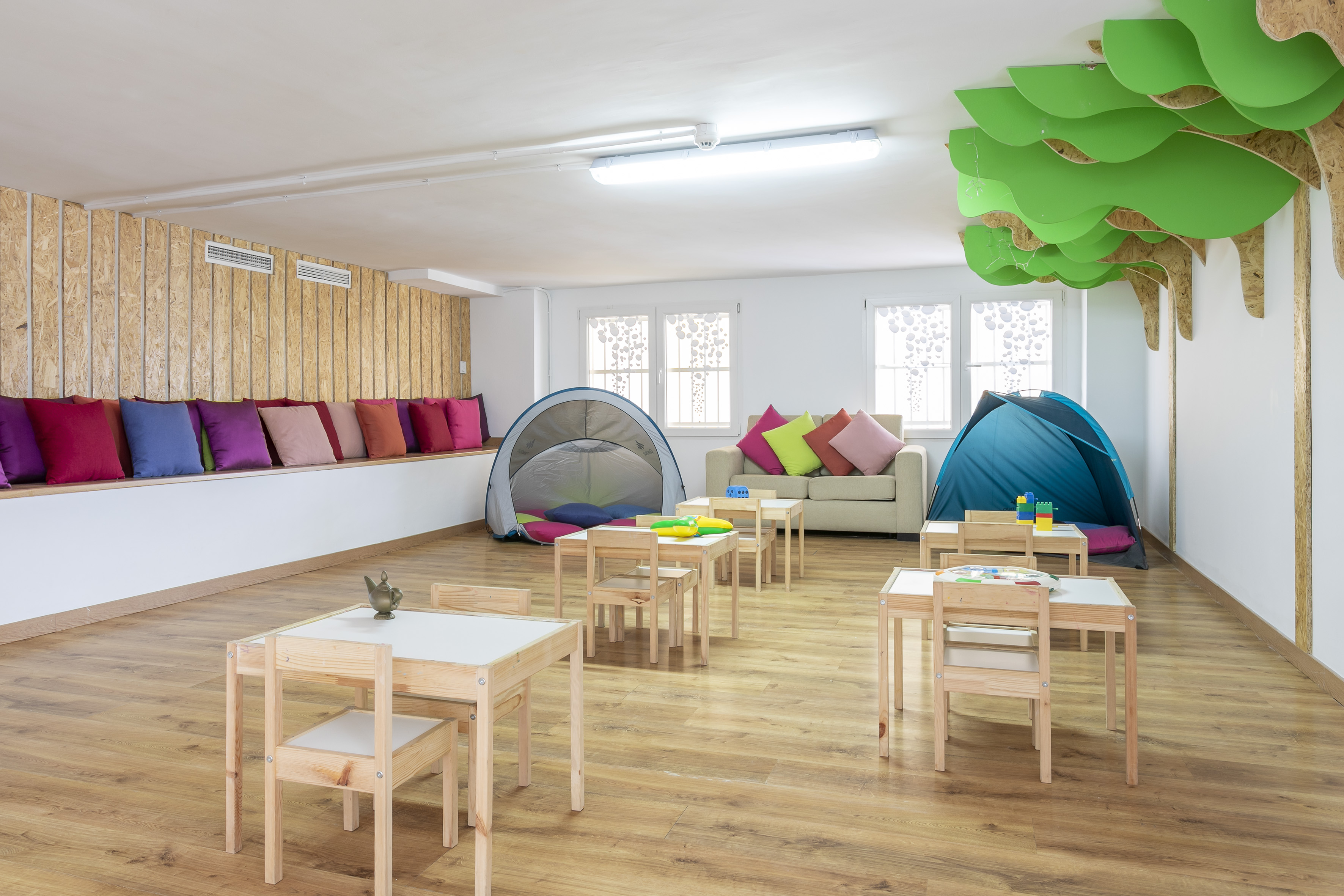 Colorful kids' play area with small tables, tents, and whimsical tree decor.