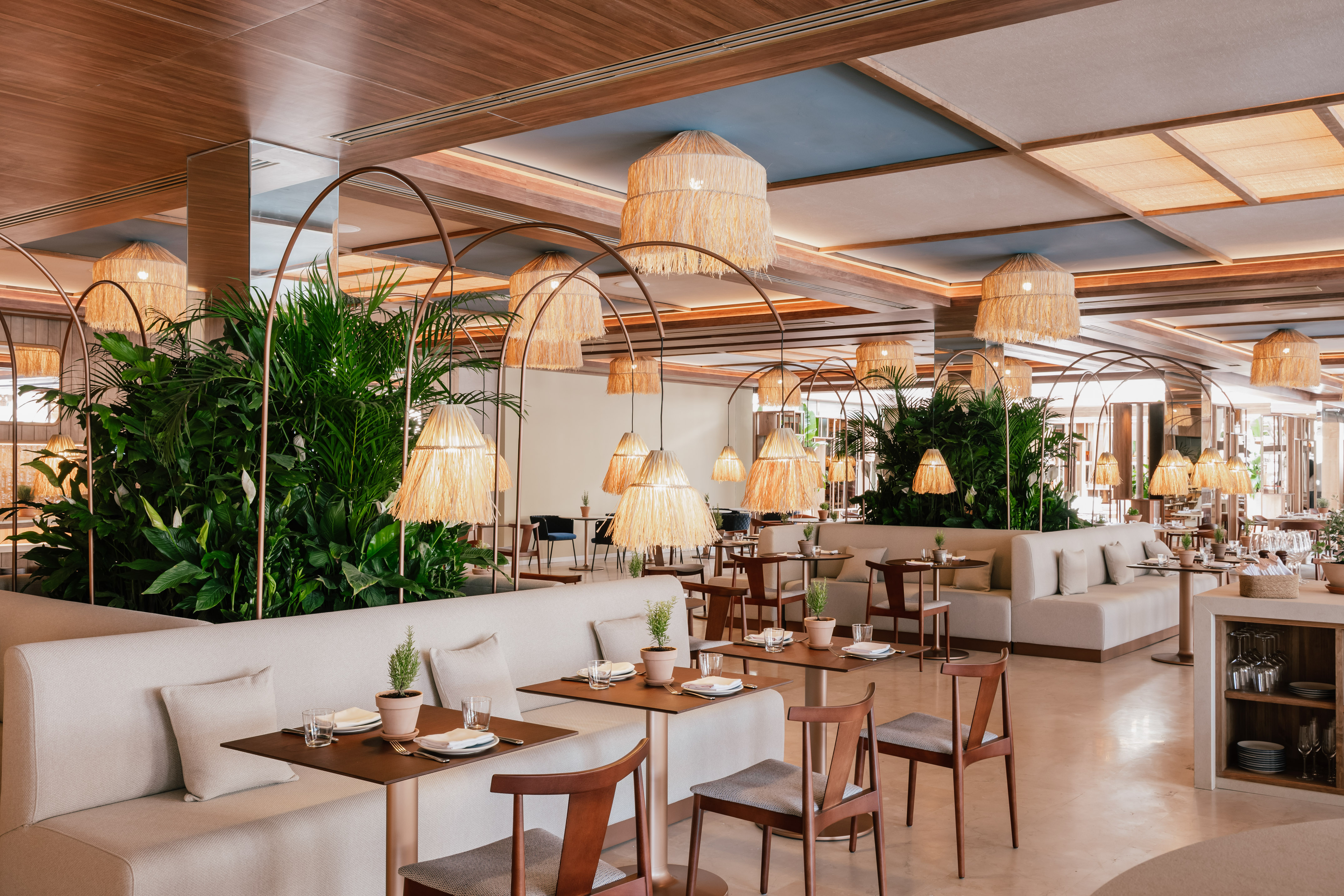 Modern dining room with green plants, natural wood, and straw pendant lights.