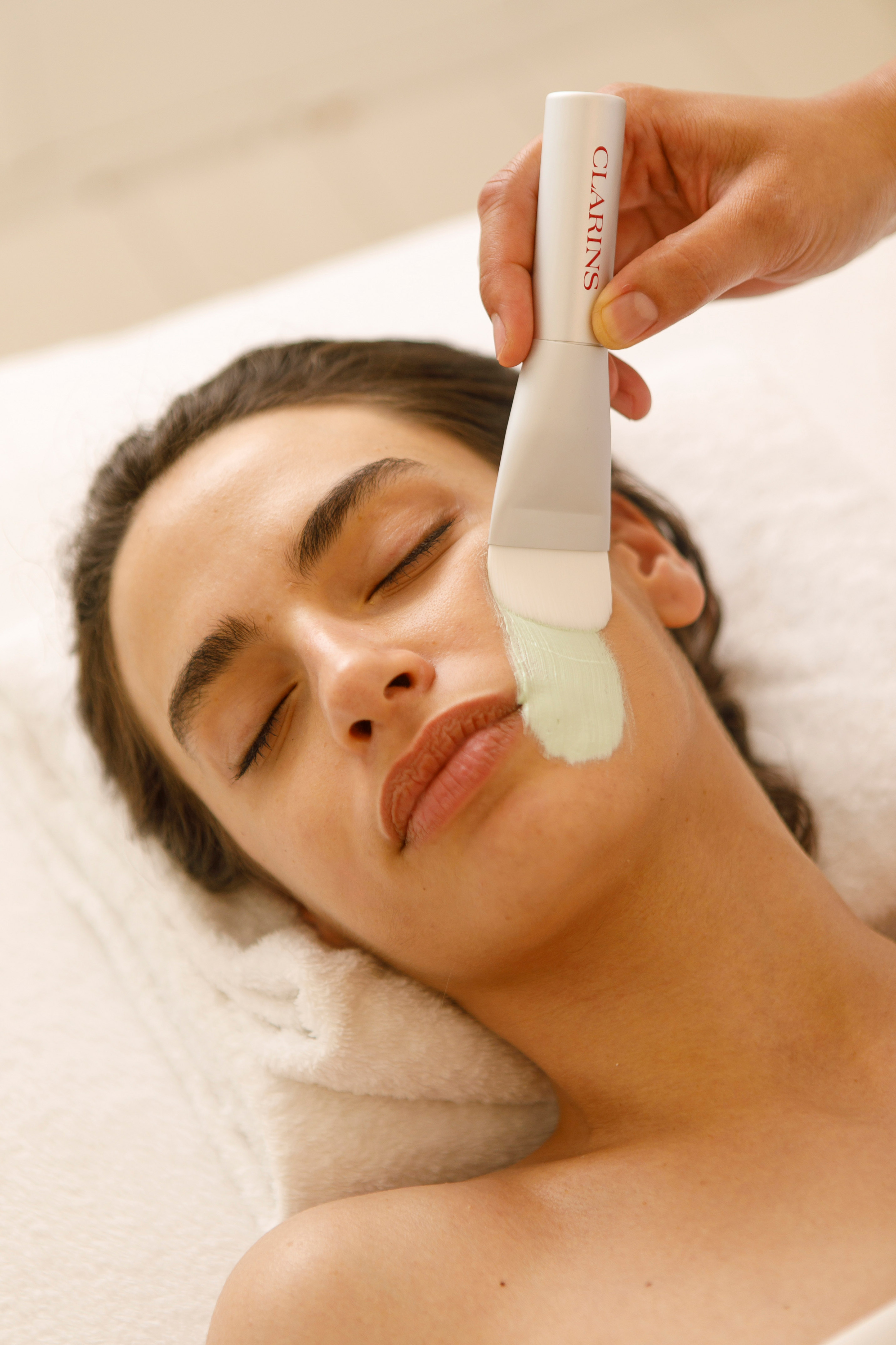 Clarins face mask application with brush on woman's cheek for skincare.