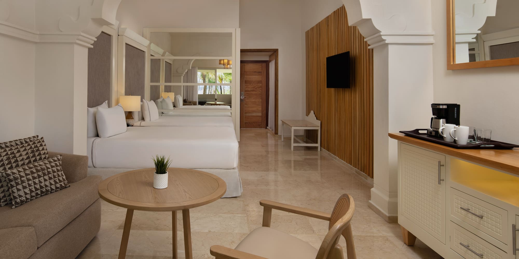 Luxurious hotel room with two beds, sofa, coffee maker, and modern design.