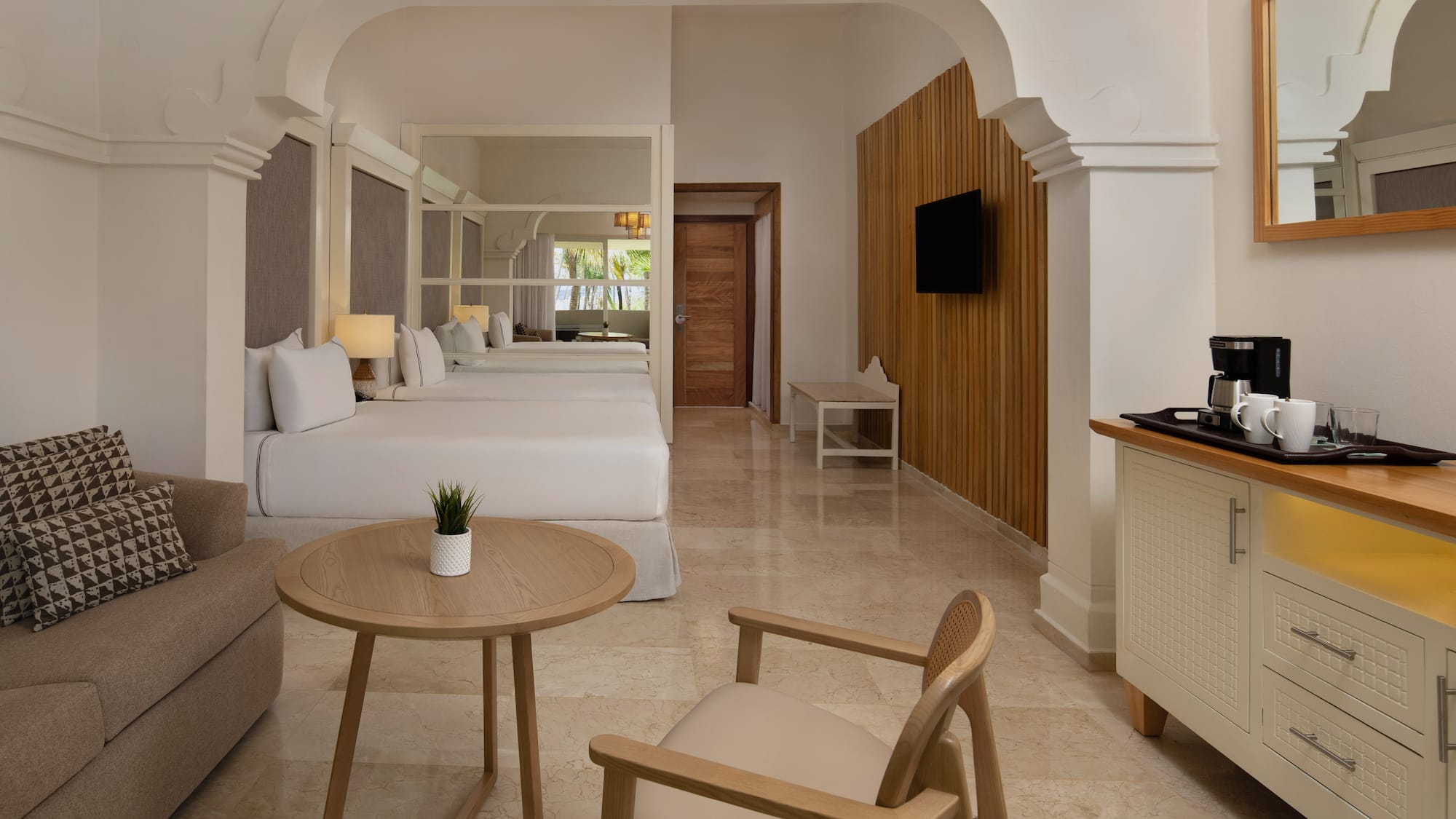 Luxurious hotel room with two beds, sofa, coffee maker, and modern design.