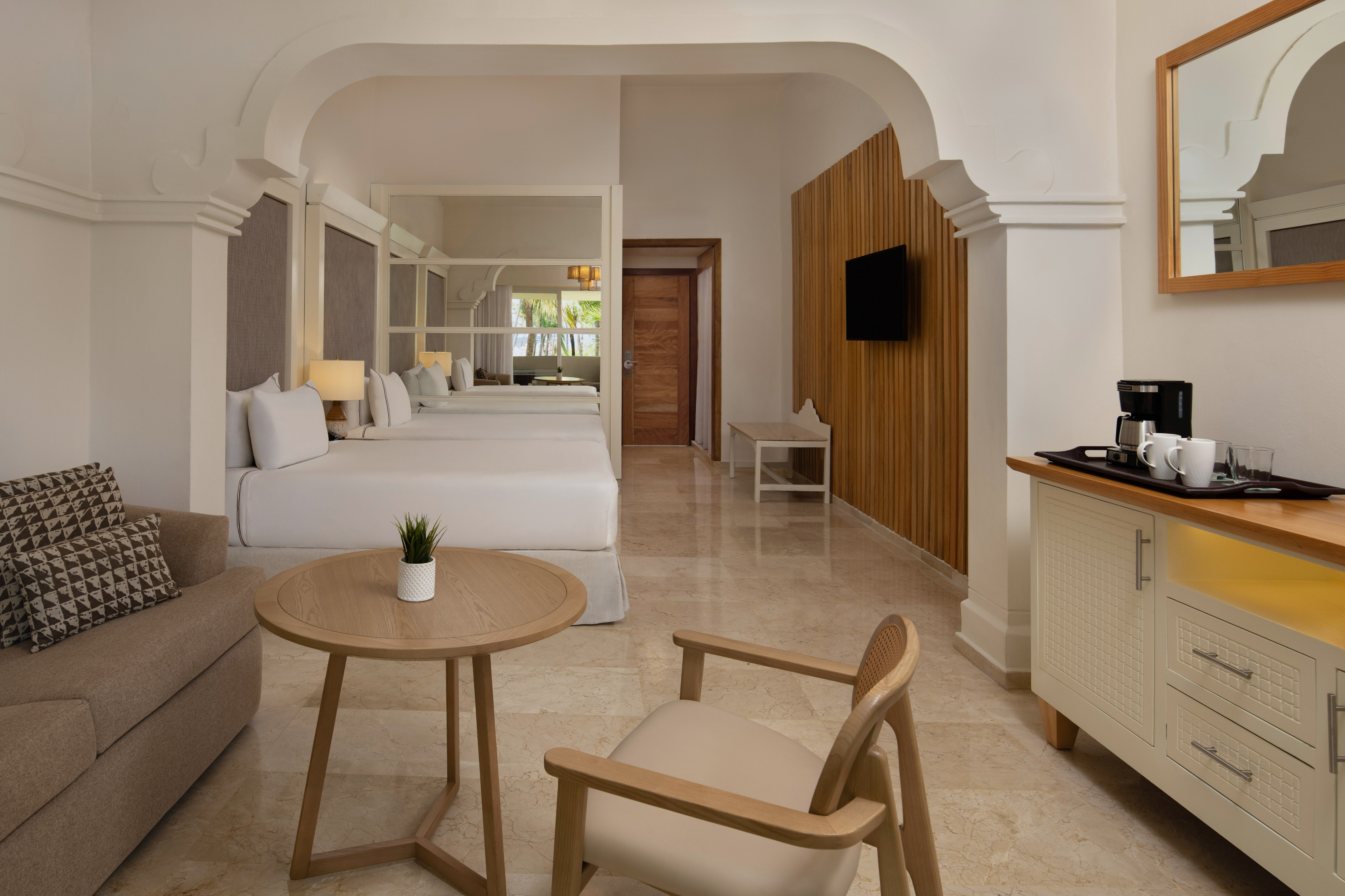 Luxurious hotel room with two beds, sofa, coffee maker, and modern design.
