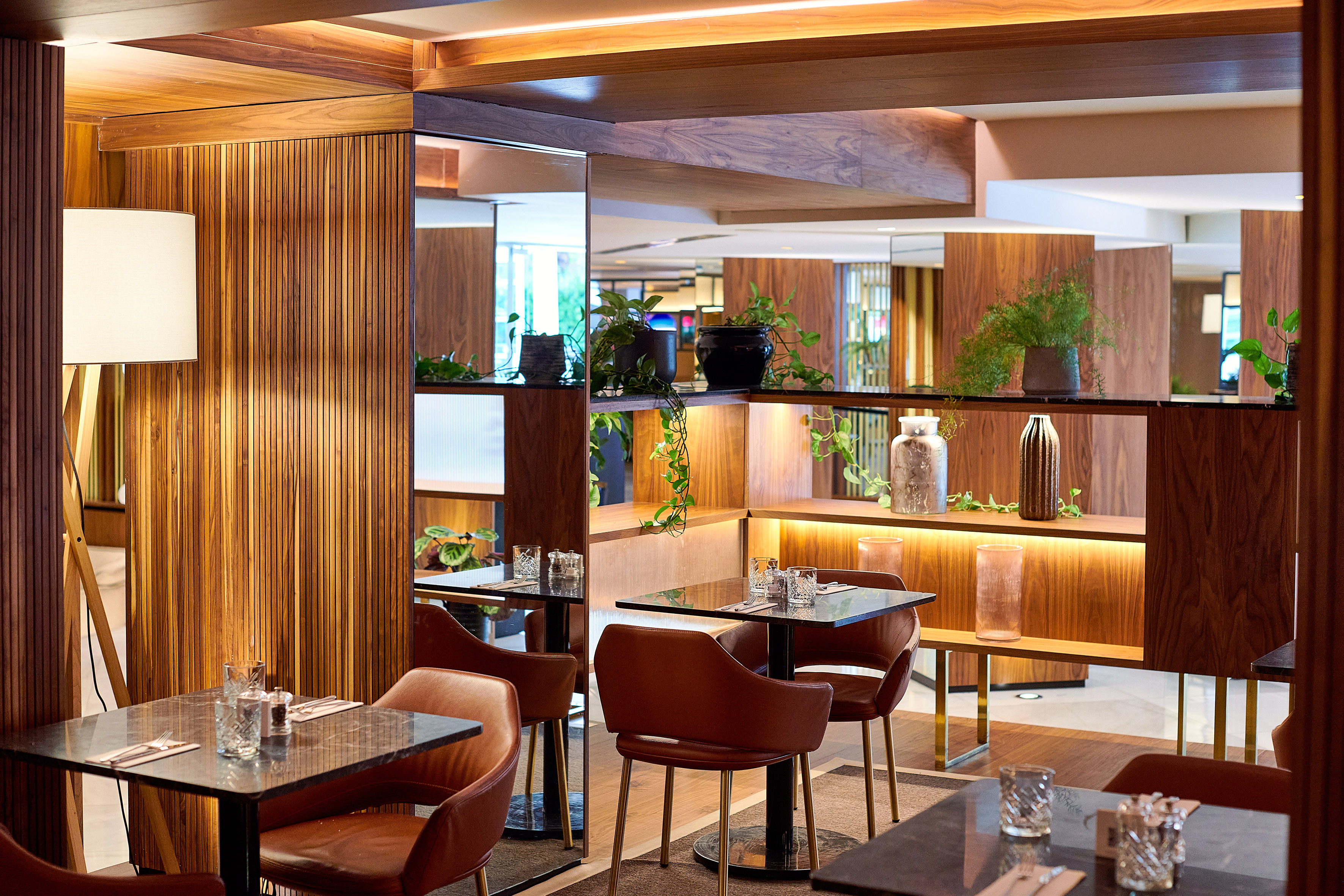Modern restaurant with wooden interiors, dining tables, and lush green plants.