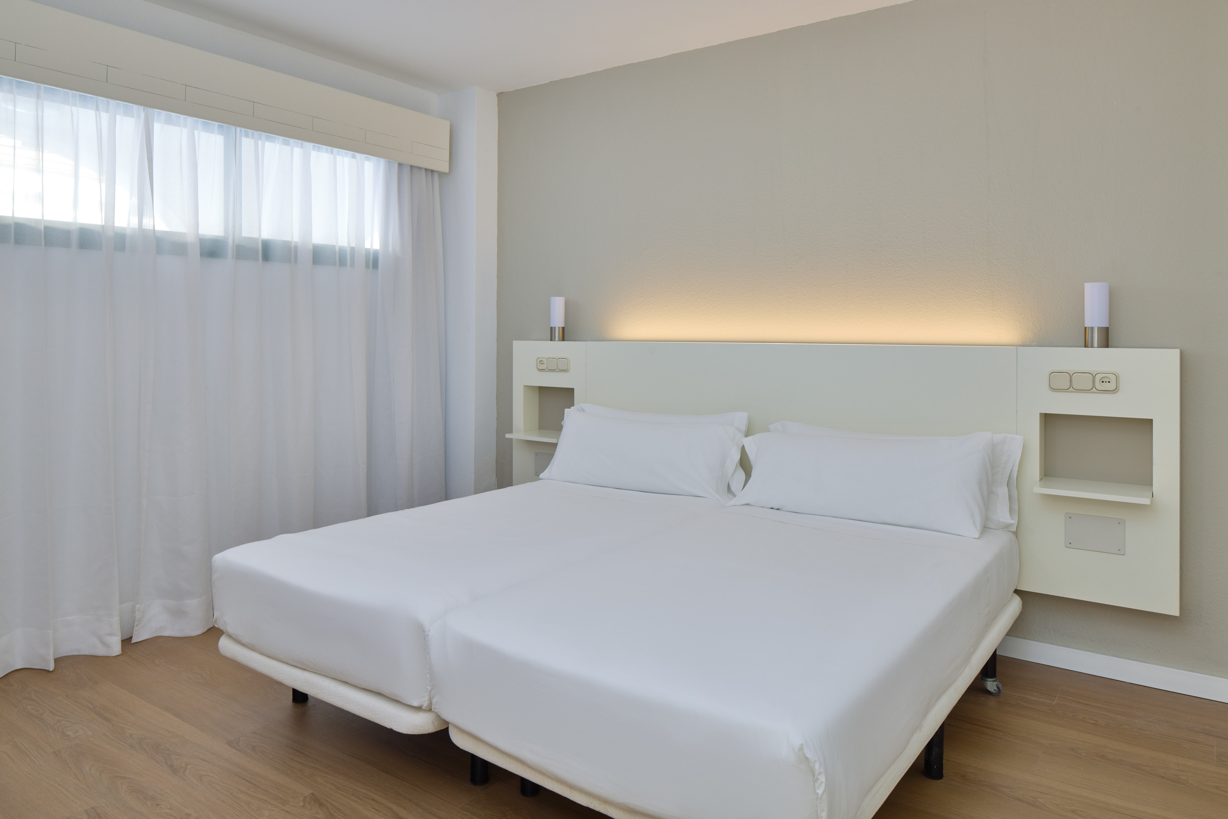 Clean hotel bedroom with two single beds, white linens, and illuminated headboard.