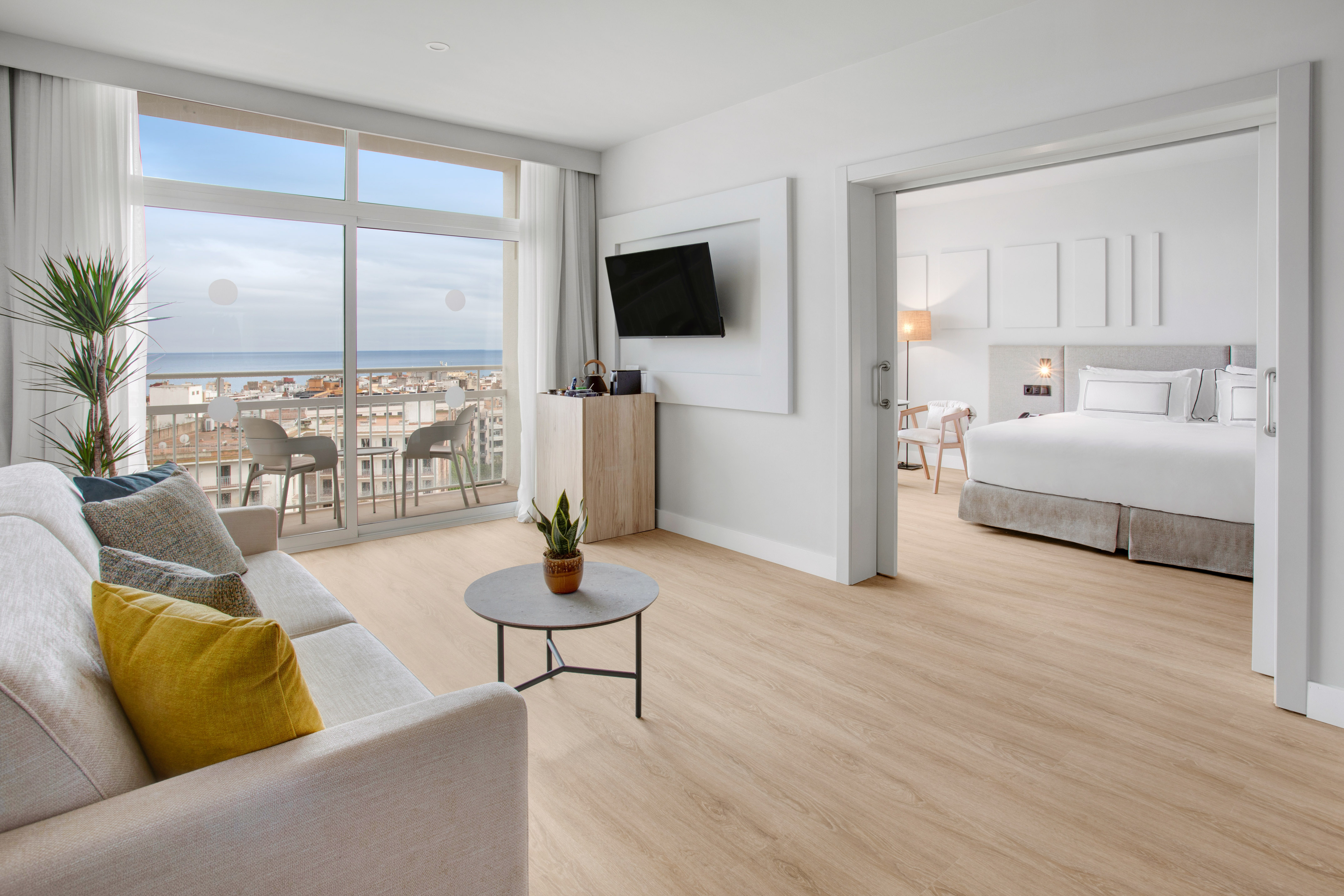 Modern hotel suite with living area, sea view balcony, and connecting bedroom.