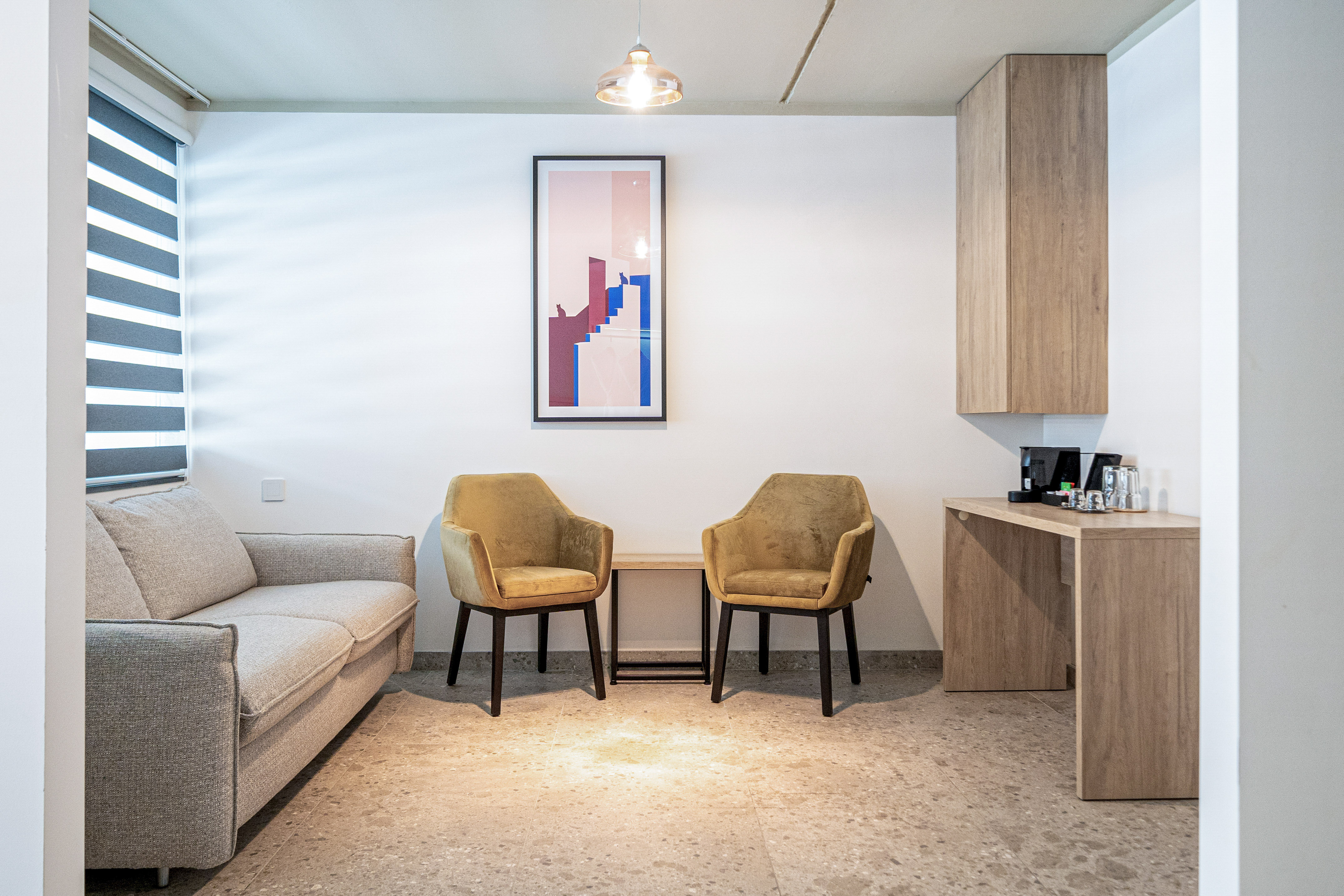 Modern living room with sofa, yellow armchairs, abstract art, and coffee station.