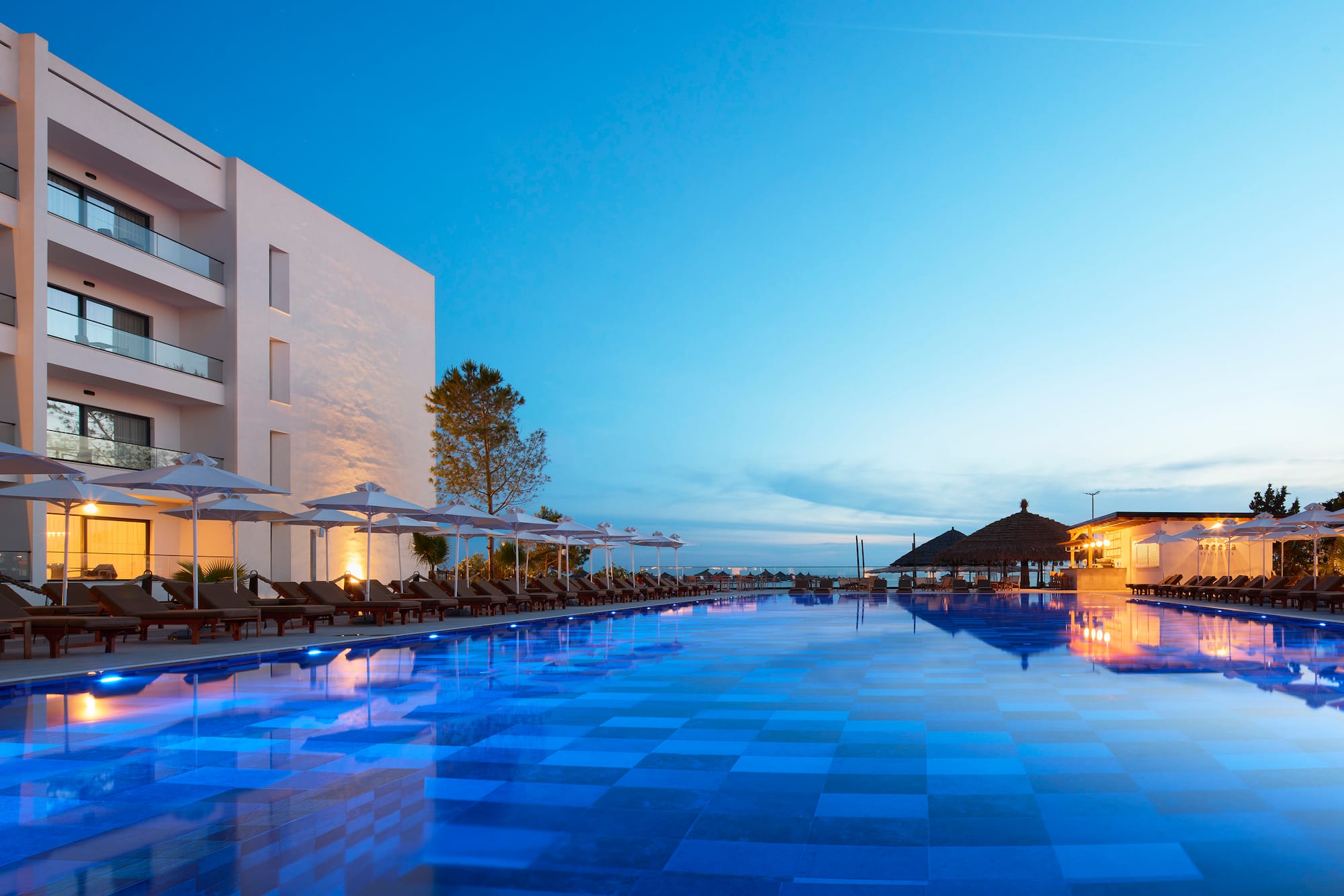 Luxury resort evening with large blue glowing swimming pool and modern hotel.