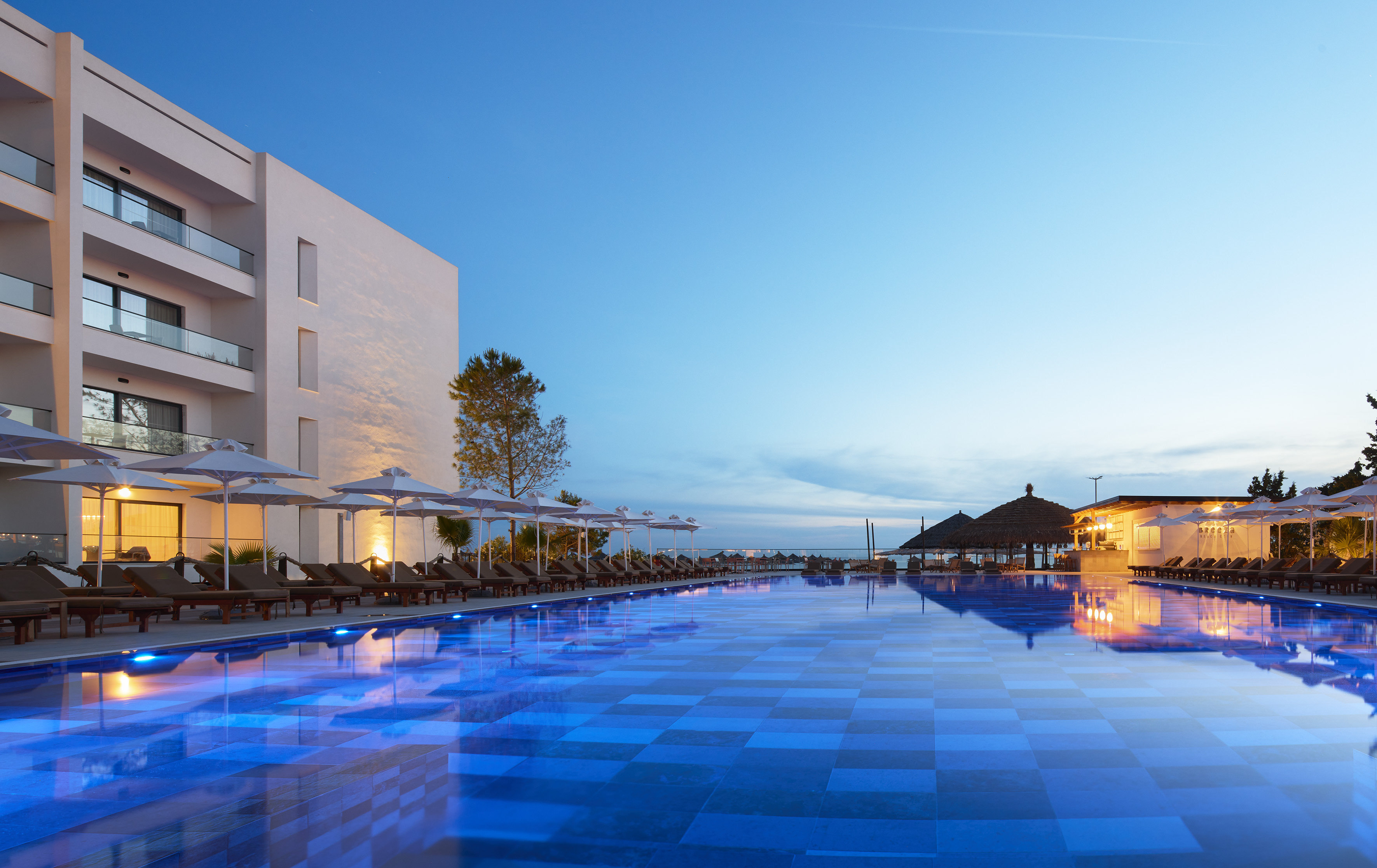 Luxury resort evening with large blue glowing swimming pool and modern hotel.