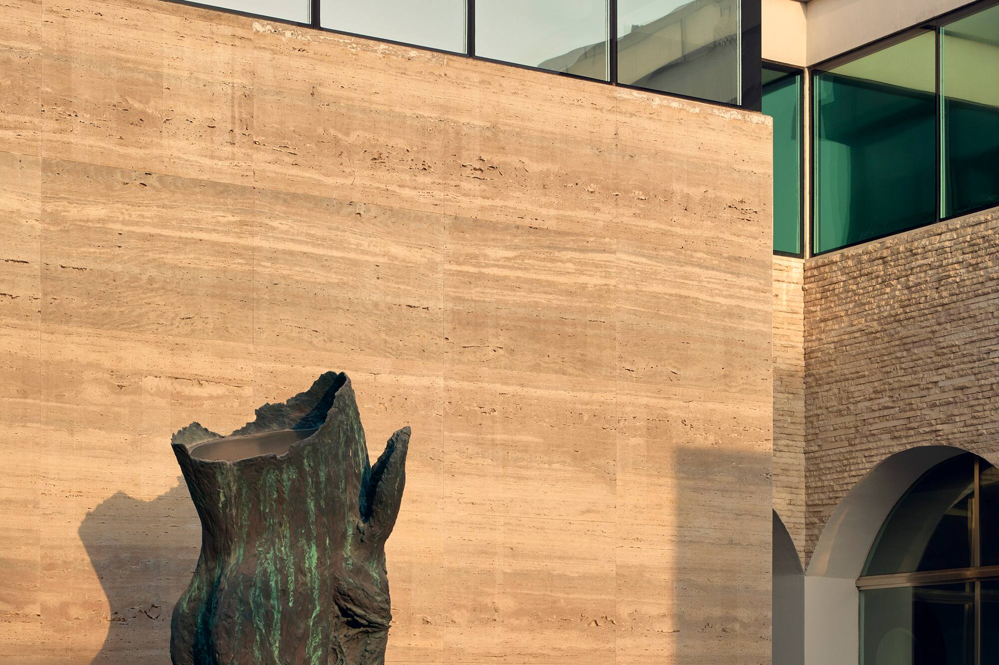 Modern building facade featuring abstract bronze fountain, stone wall, and glass.
