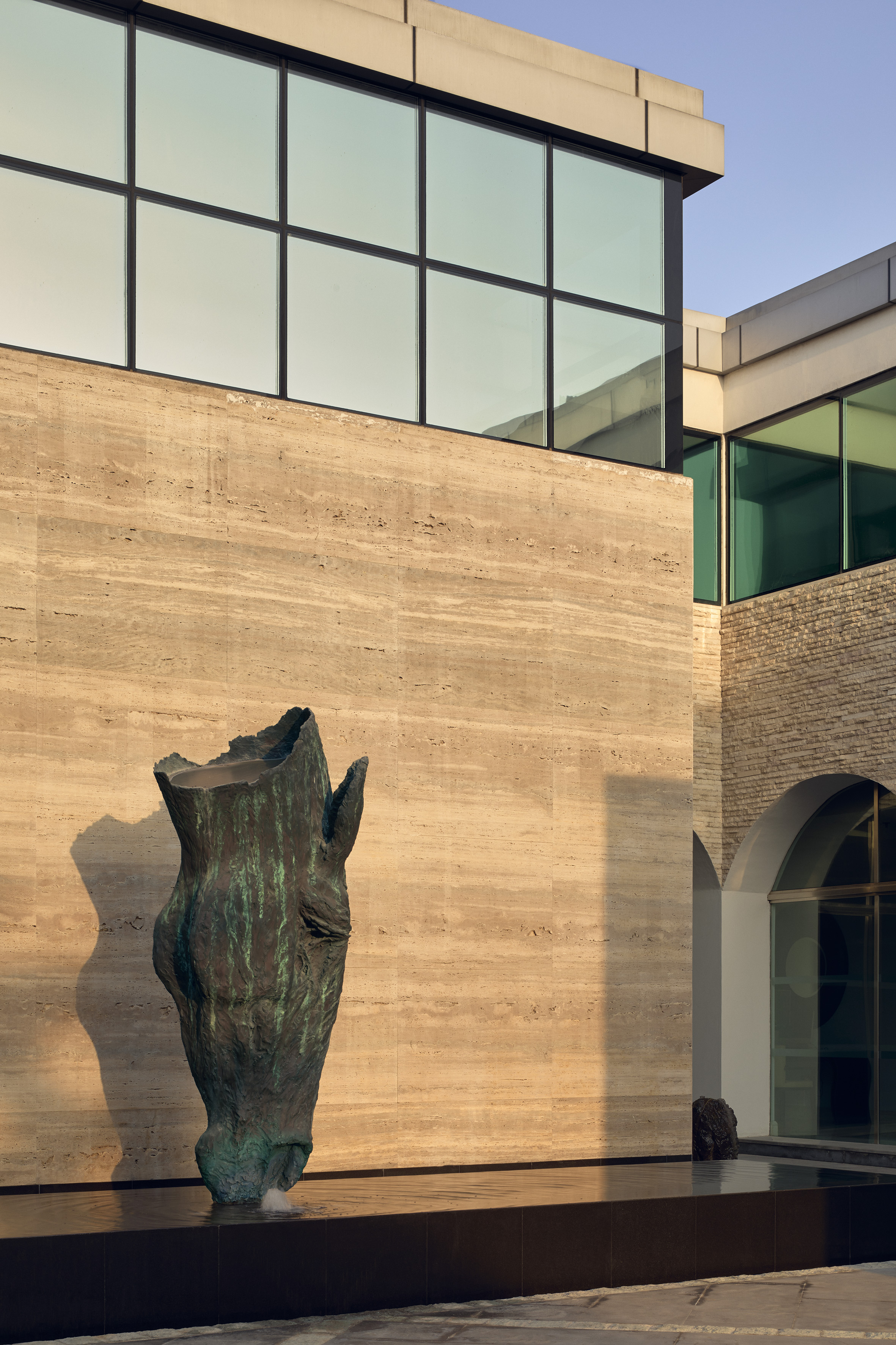 Modern building facade featuring abstract bronze fountain, stone wall, and glass.