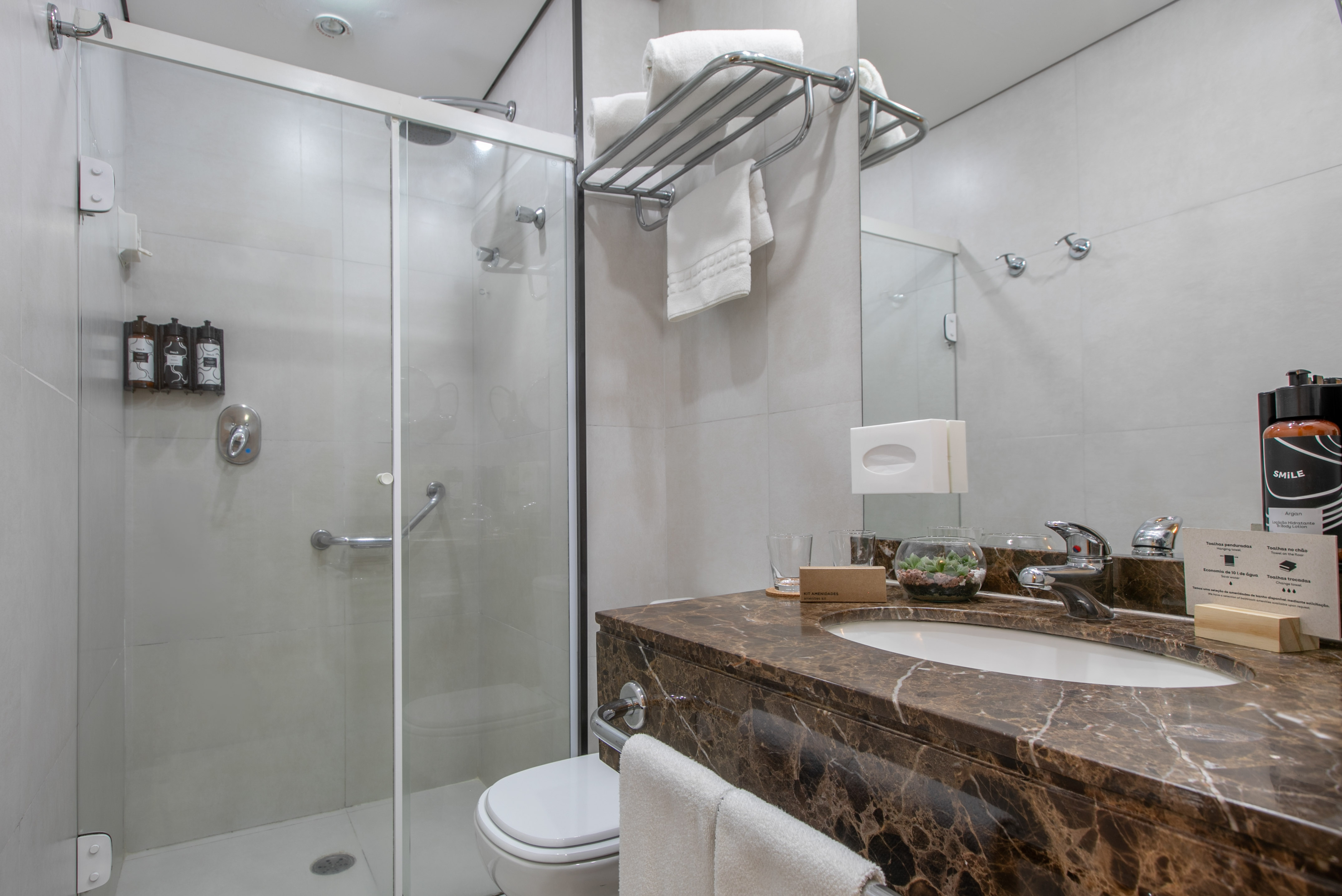 Clean hotel bathroom with glass shower, marble vanity, sink, toilet, and amenities.