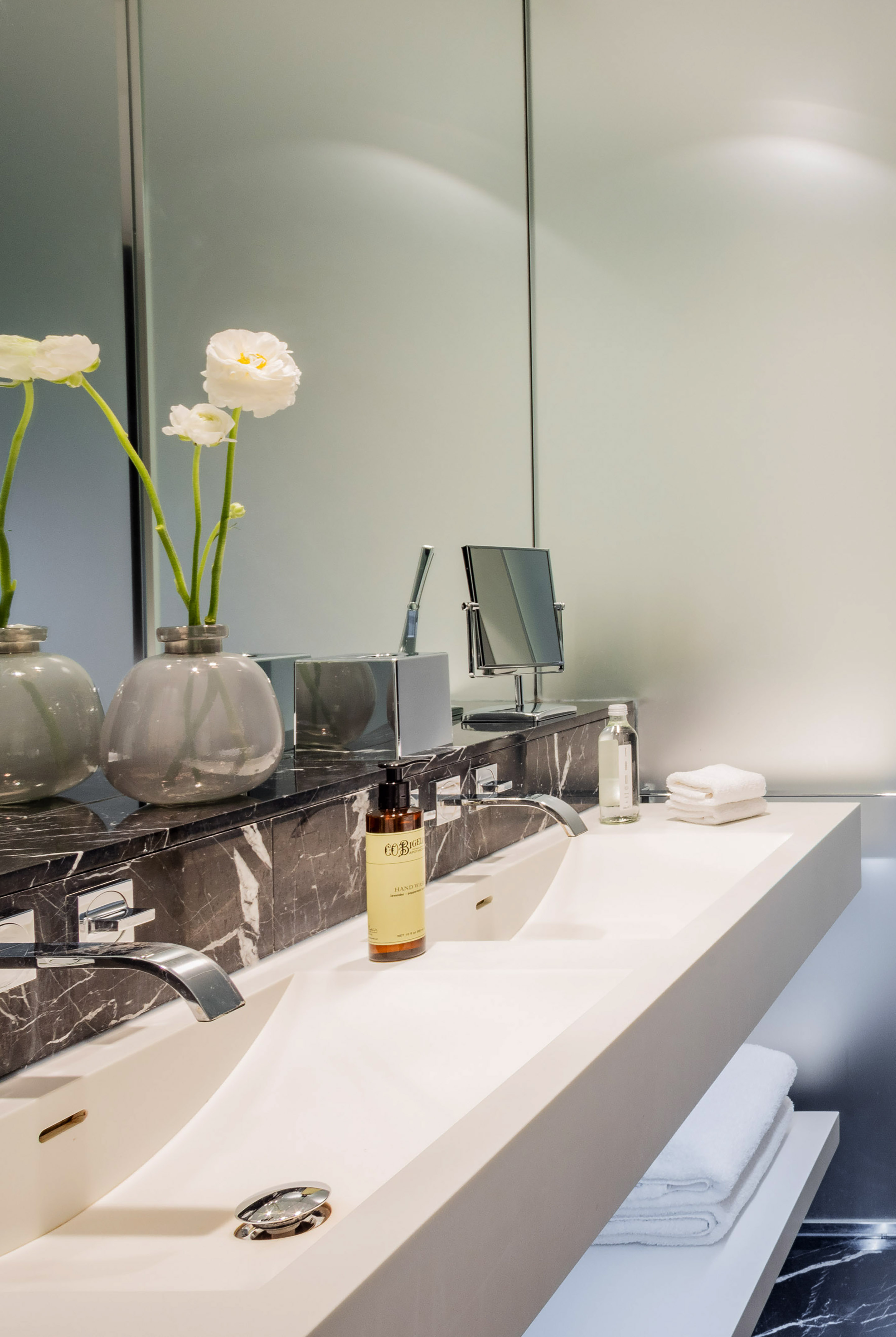 Modern bathroom vanity with double sinks, black marble, white flowers, and toiletries.