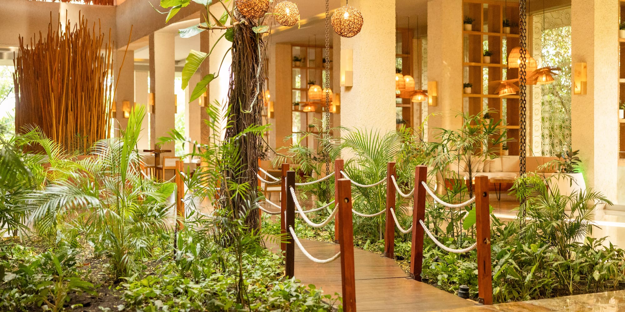 Lush indoor garden walkway in a tropical resort lobby with warm lighting.