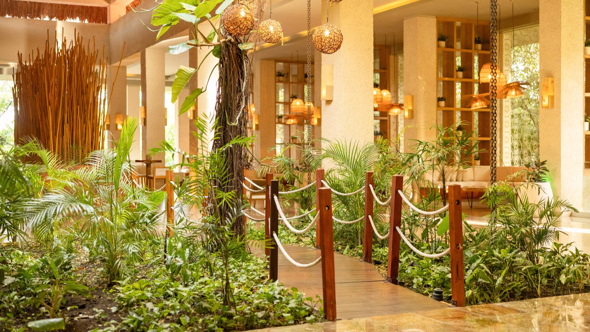 Lush indoor garden walkway in a tropical resort lobby with warm lighting.