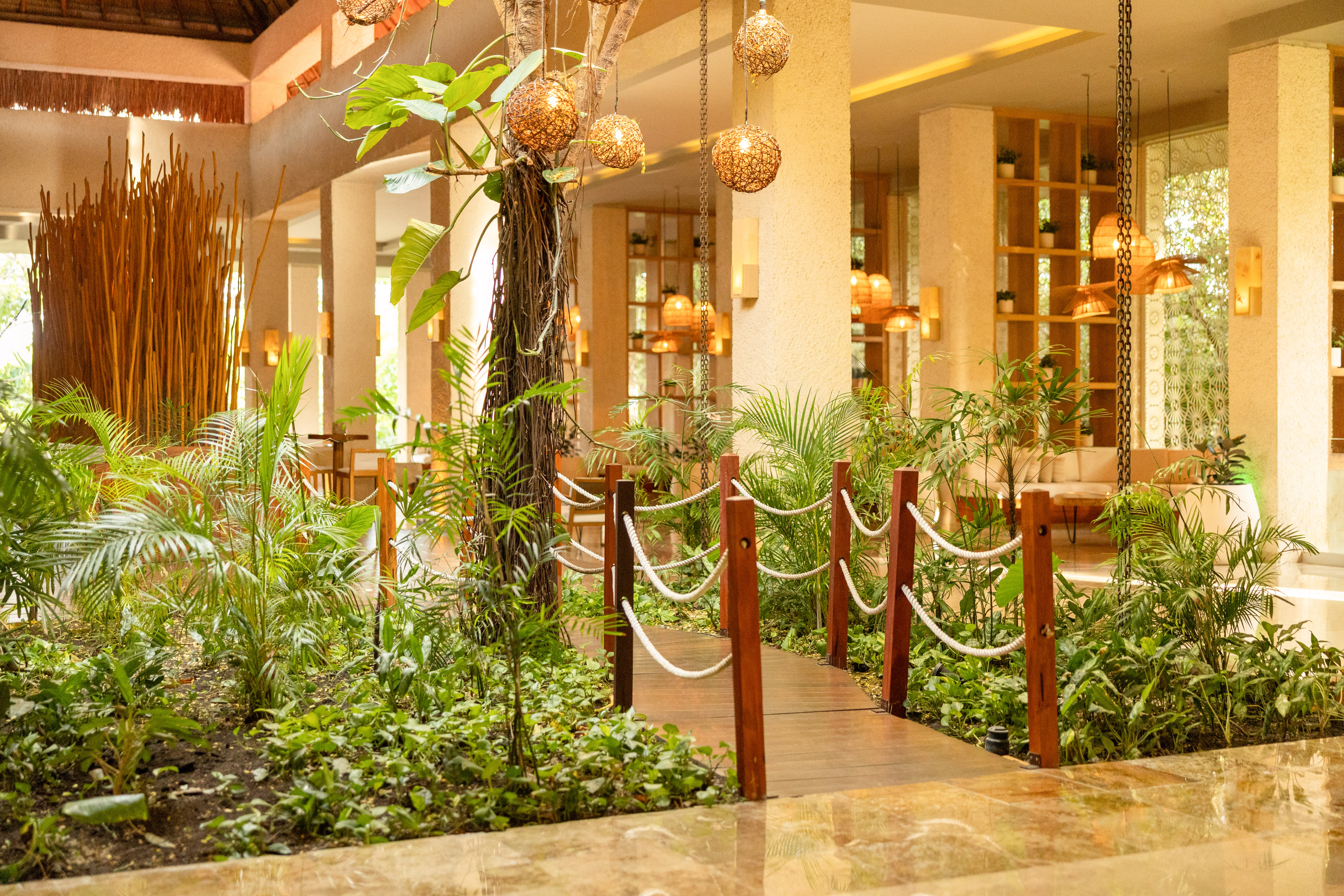 Lush indoor garden walkway in a tropical resort lobby with warm lighting.