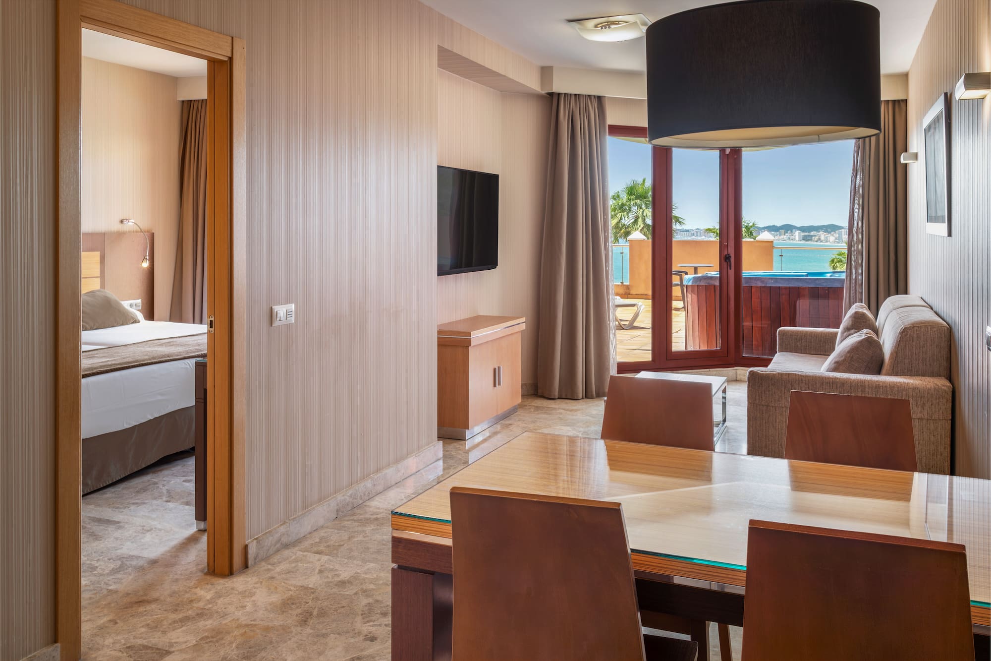Hotel suite with living room, bedroom, and ocean view balcony with hot tub.