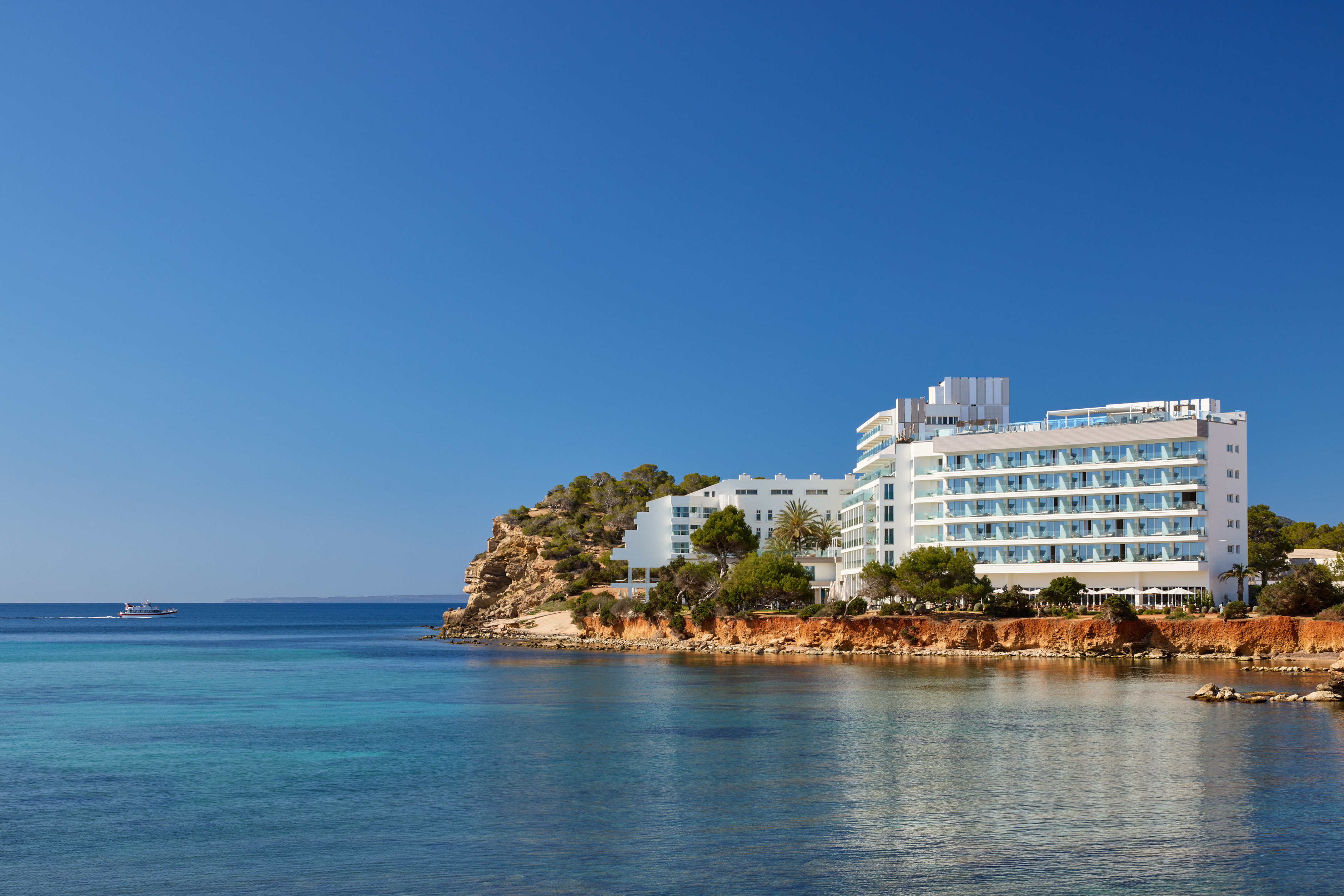 Modern white hotel resort on a cliff overlooking clear turquoise sea.