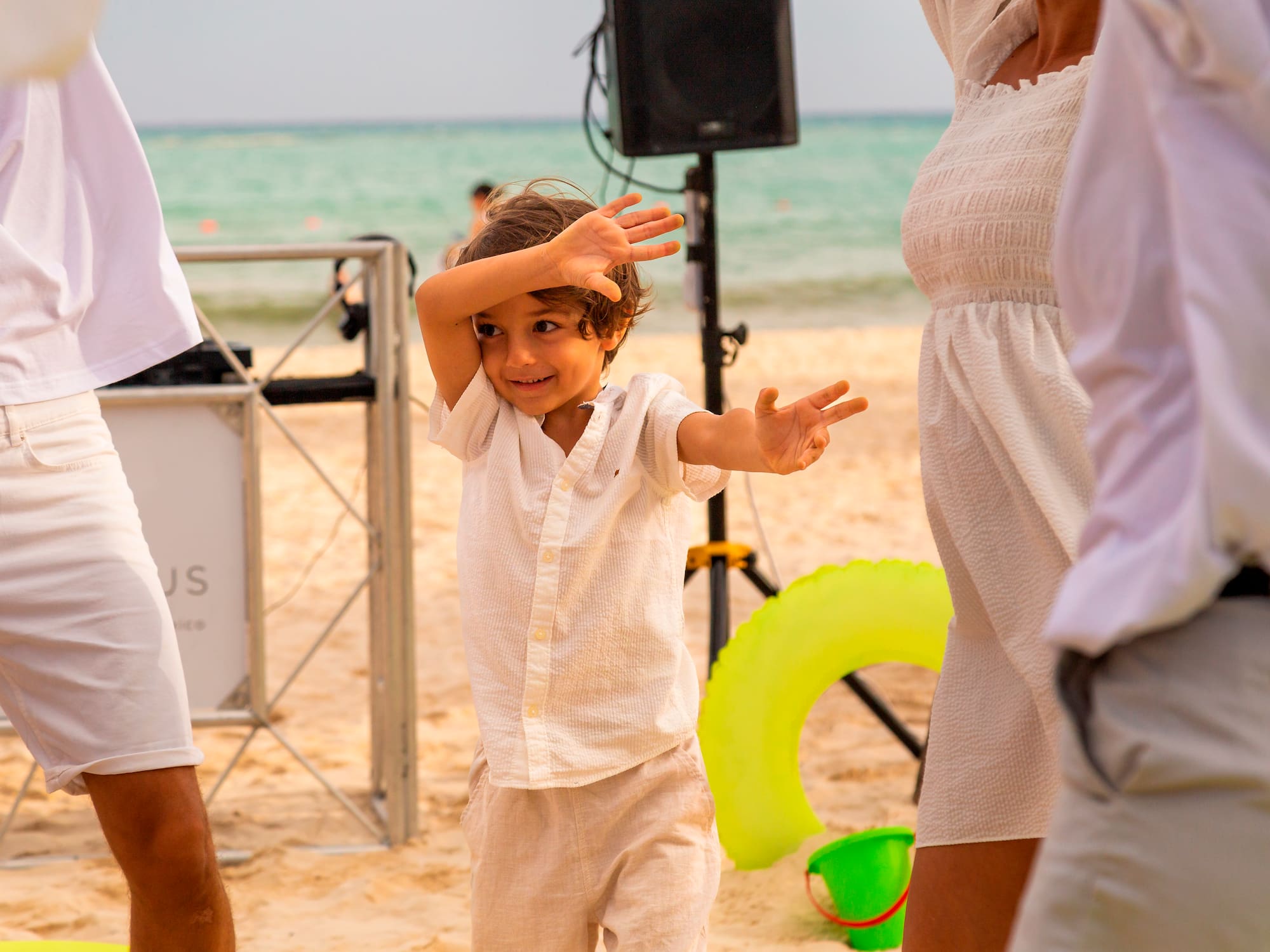 a child with hands up in front of a woman and a man on a beach