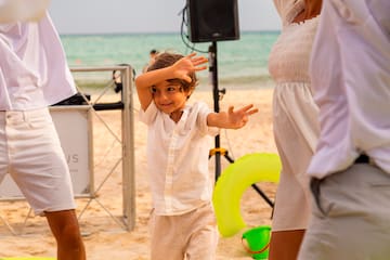 a child with hands up in front of a woman and a man on a beach