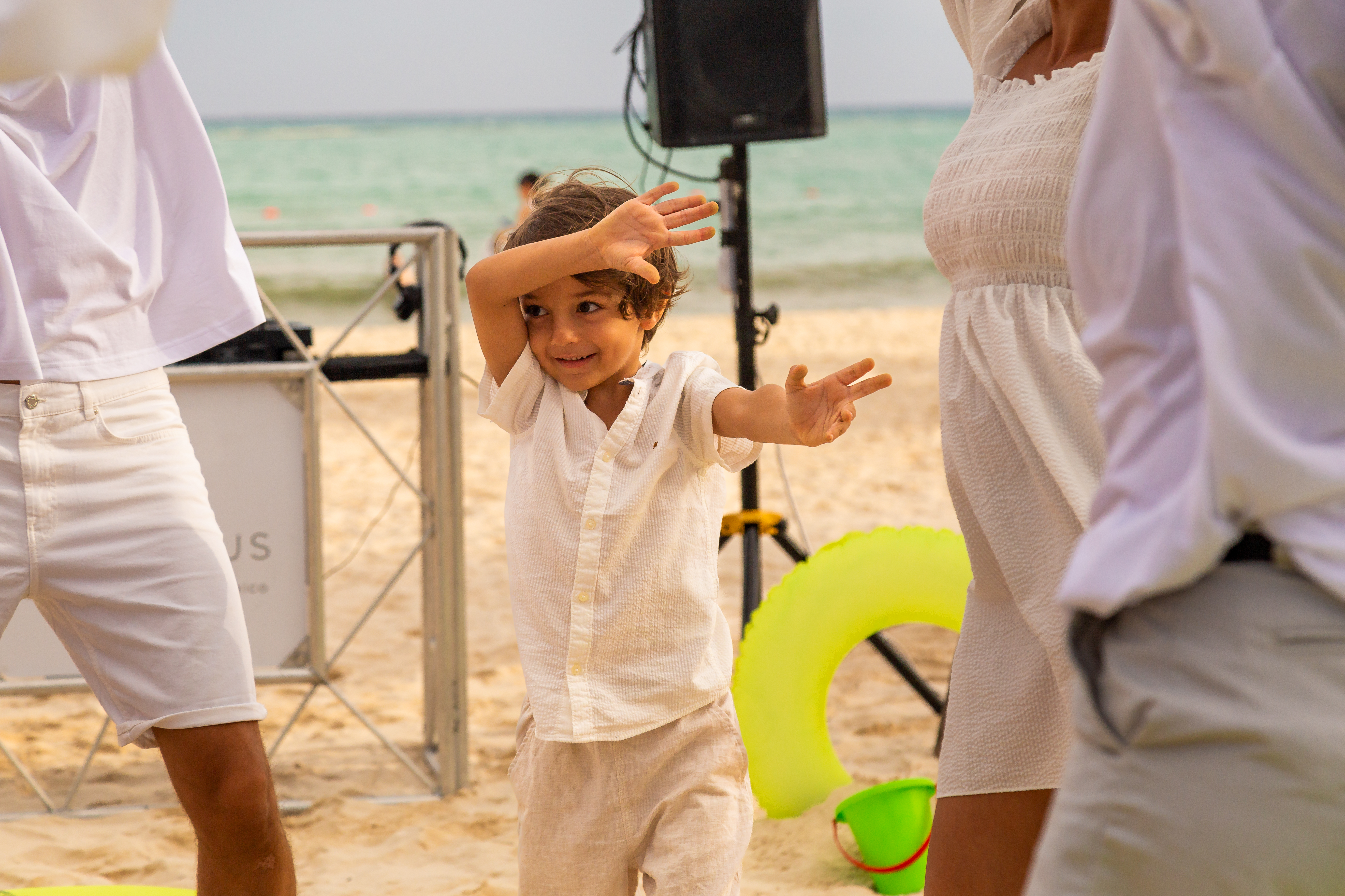 a child with hands up in front of a woman and a man on a beach