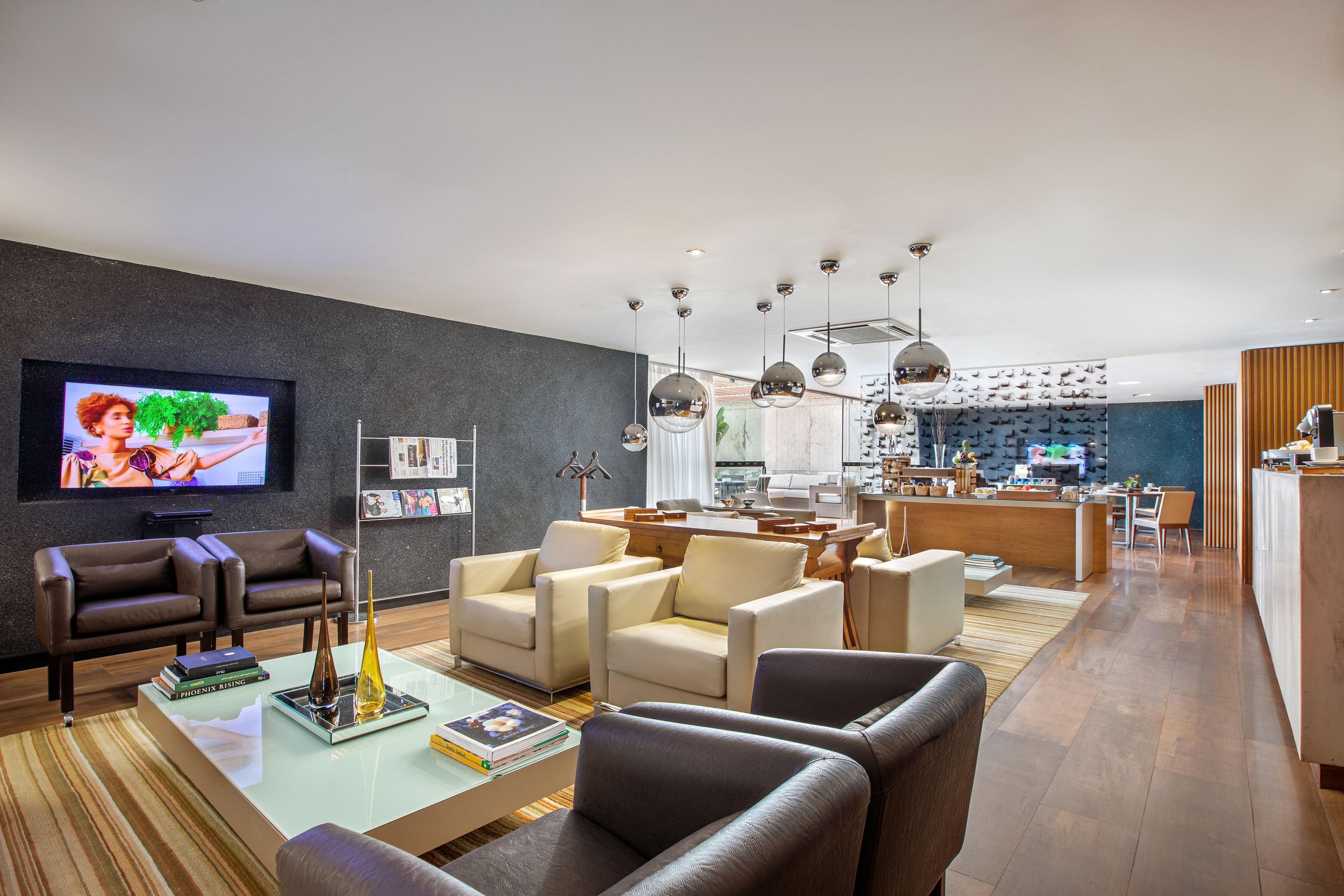 Modern lounge with TV, brown & beige armchairs, glass table.