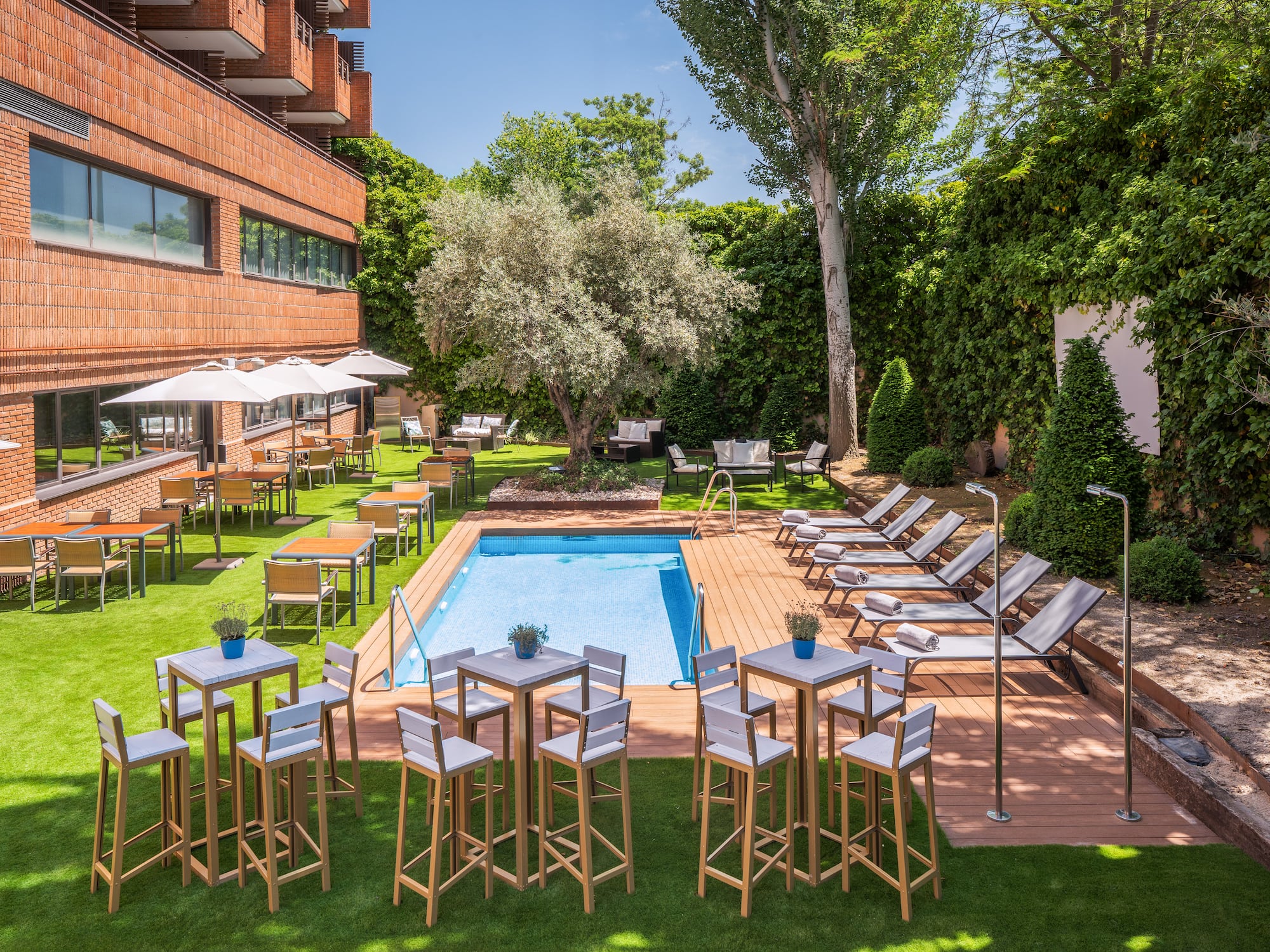 Hotel garden with swimming pool, sun loungers, and outdoor dining tables.