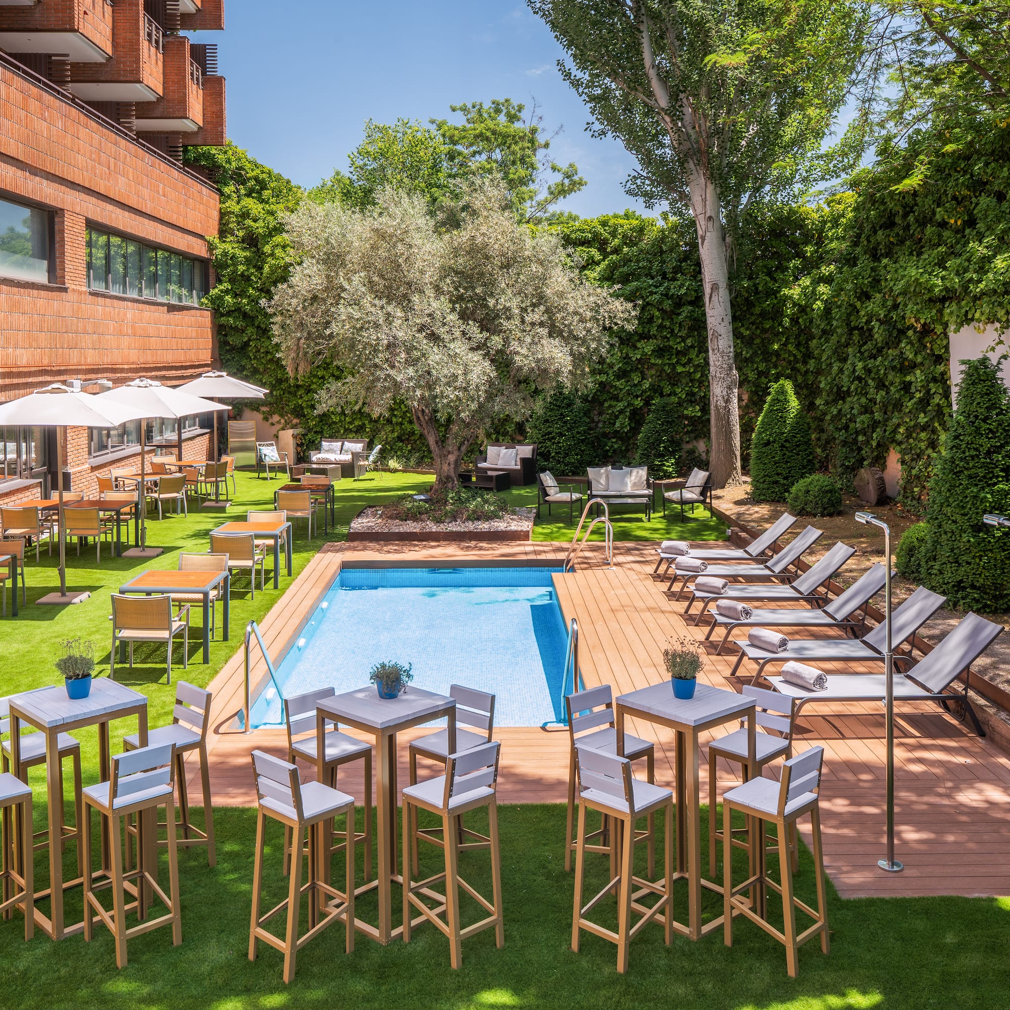 Hotel outdoor pool with sun loungers, alfresco dining, and lush garden.