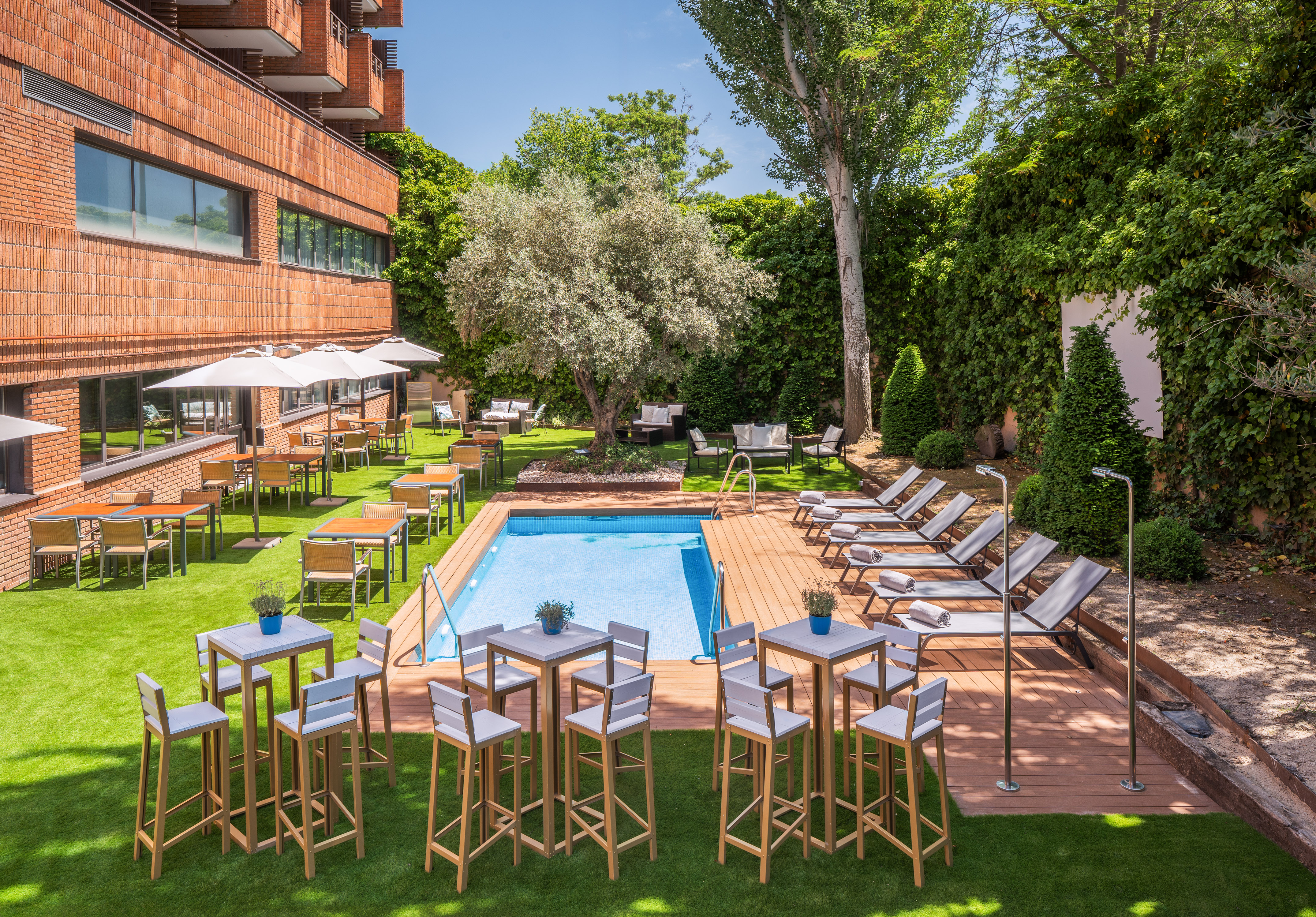 Hotel garden with swimming pool, sun loungers, and outdoor dining tables.
