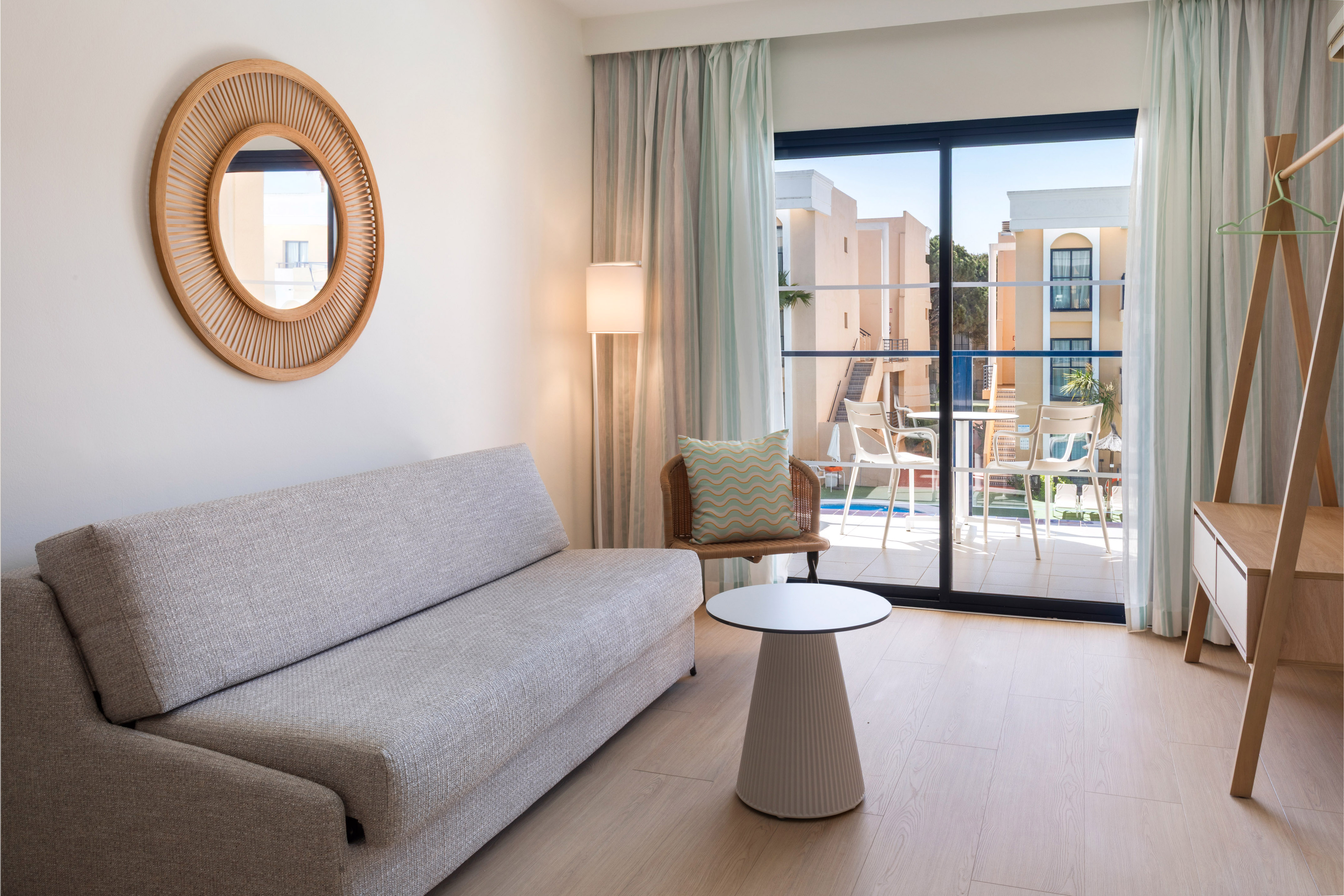 Bright modern hotel room with sofa, balcony, and resort views.