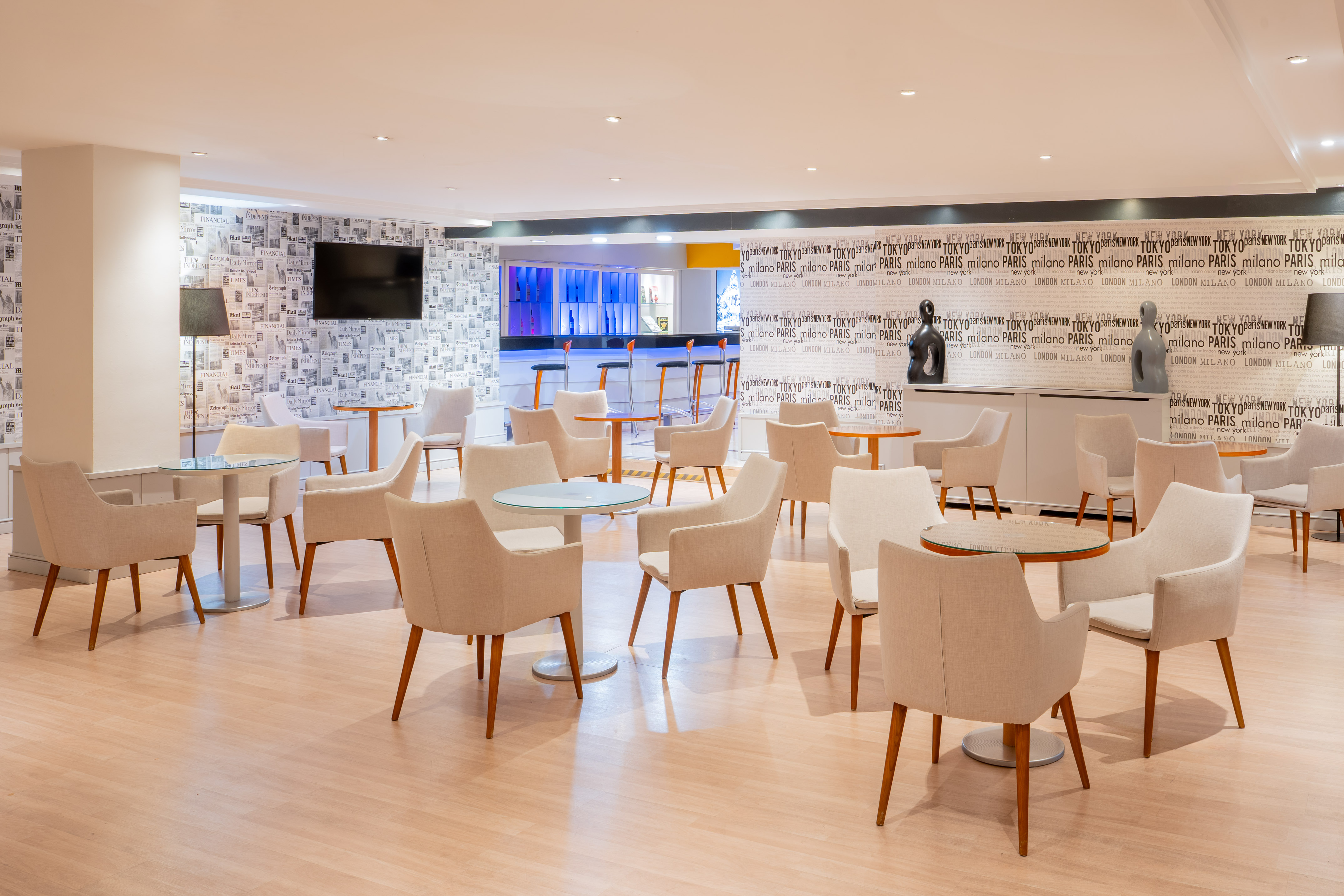 Modern lounge with comfortable seating, round tables, and city newsprint walls.