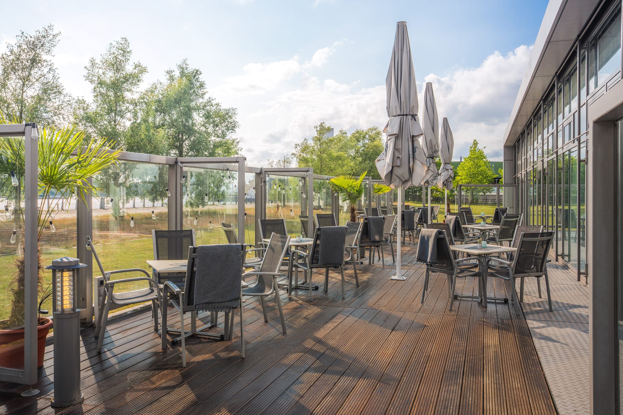 Sunny outdoor dining patio with wooden deck, tables, chairs, and umbrellas.