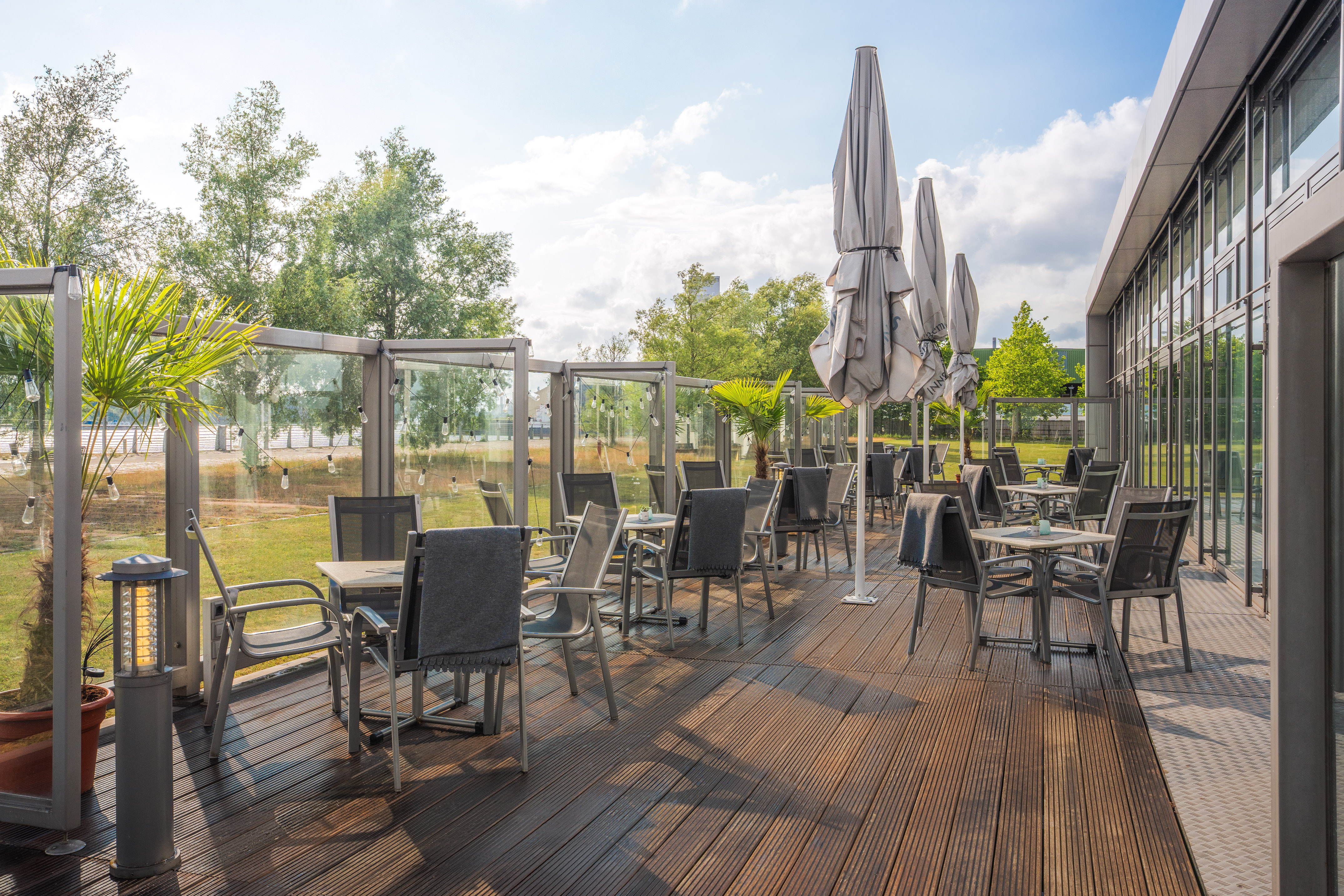 Sunny outdoor dining patio with wooden deck, tables, chairs, and umbrellas.