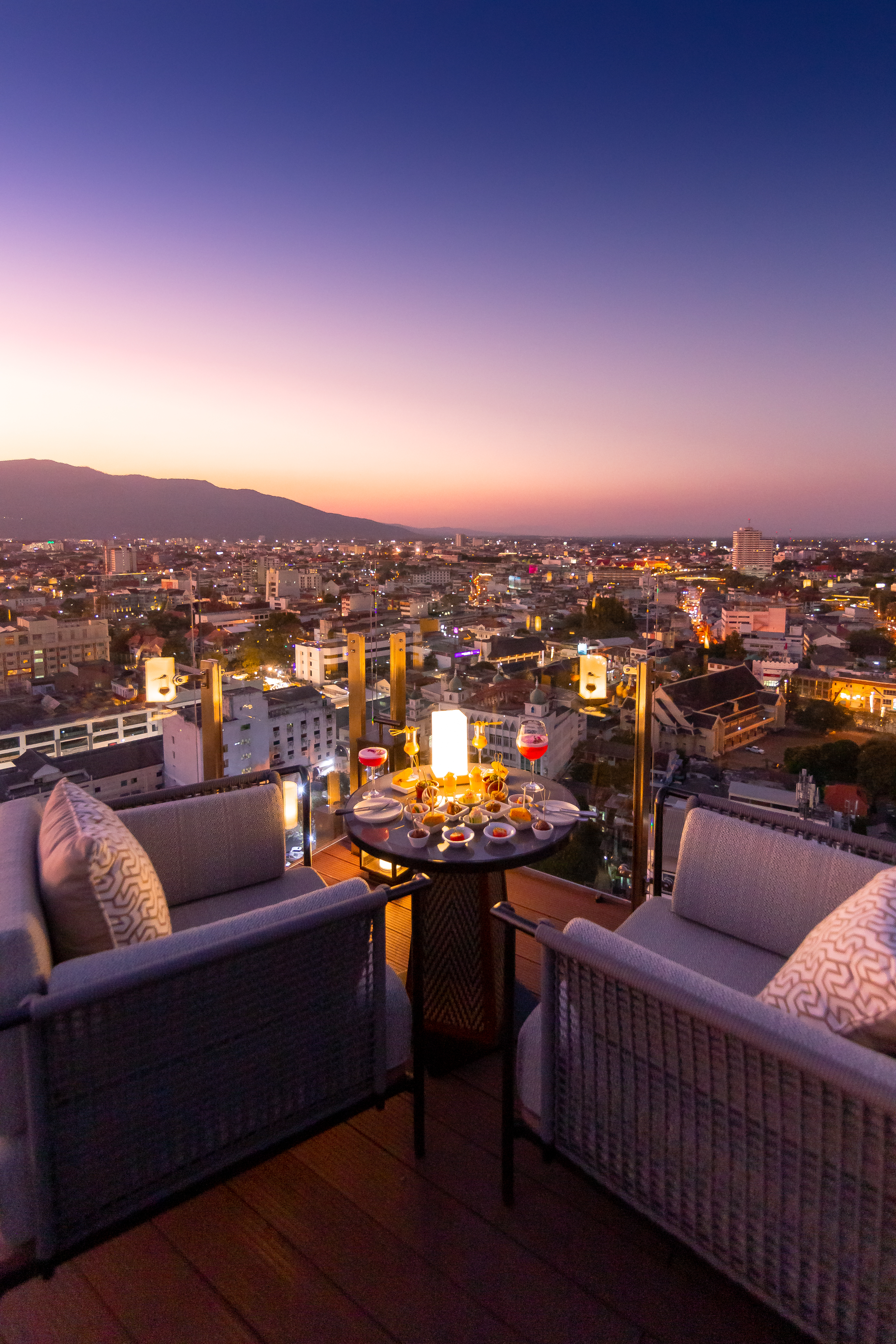 Romantic rooftop dinner overlooking city lights and mountains at sunset.