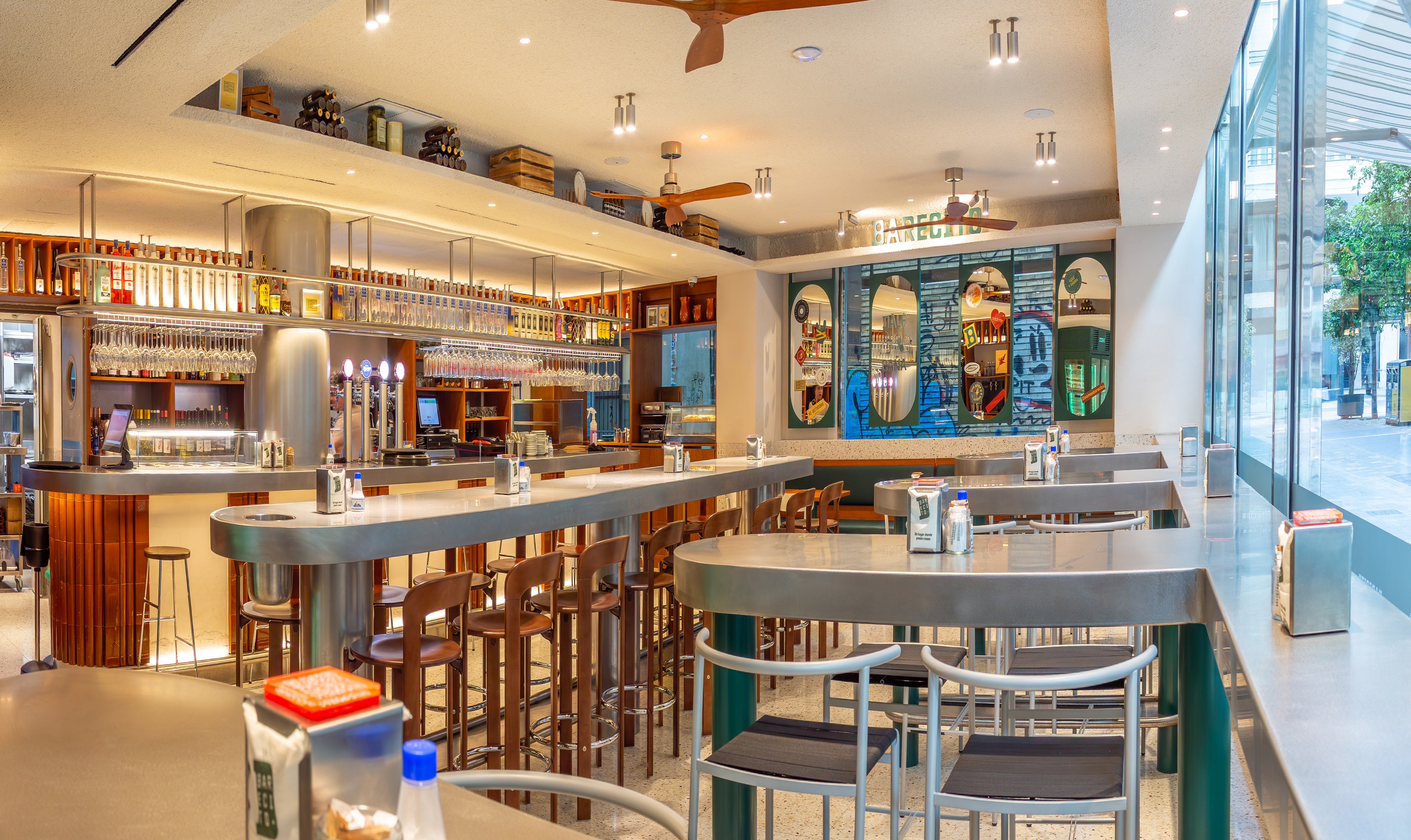 Modern bar with sleek stainless steel counter, high stools, and large windows.